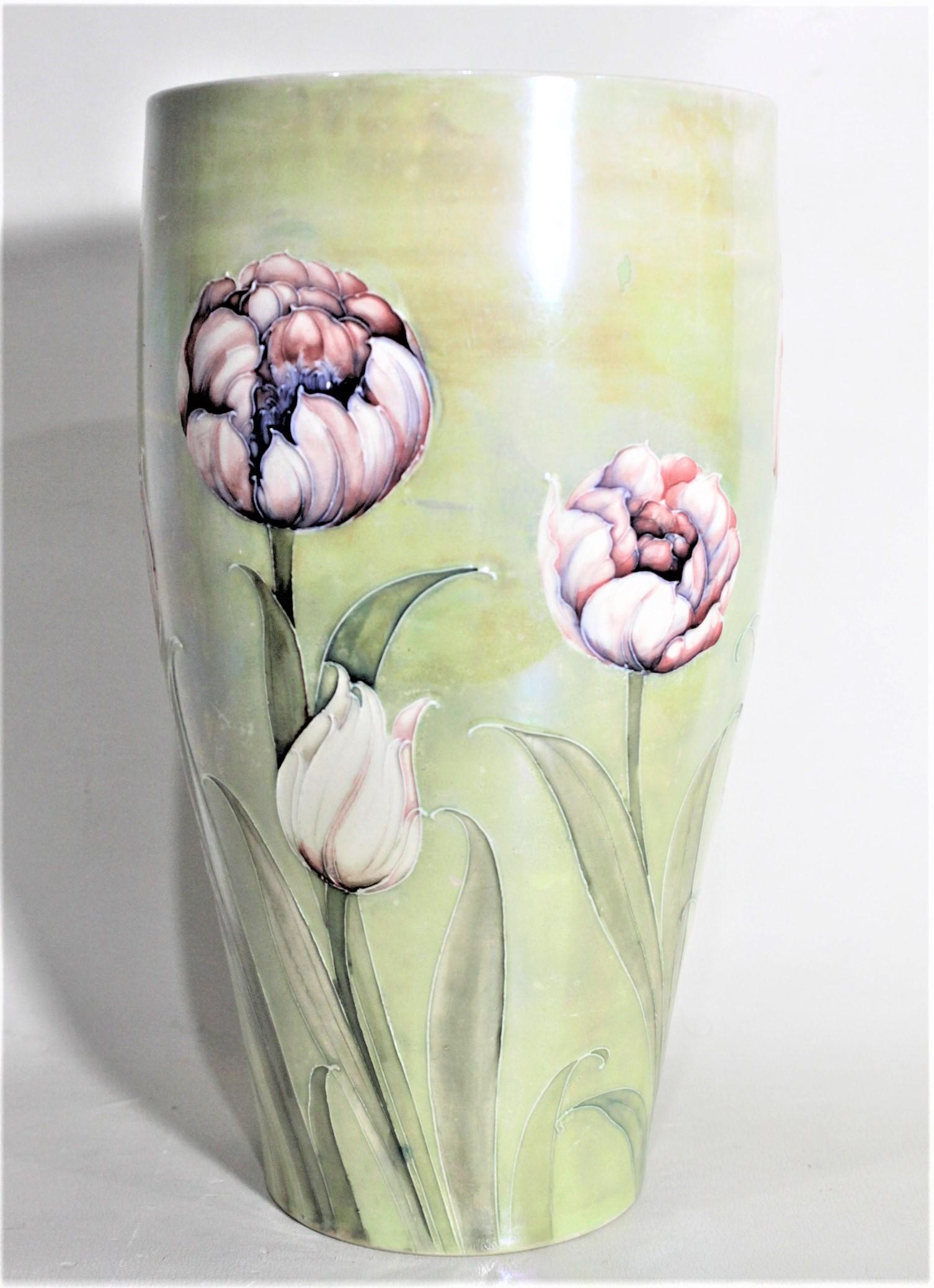 This art pottery vase was done by the Moorcroft Pottery company of England in circa 1920 with a pastel green ground with a rare tulip pattern and a light lustre over glaze. This vase may have been made for Liberty or other seller of the period as it