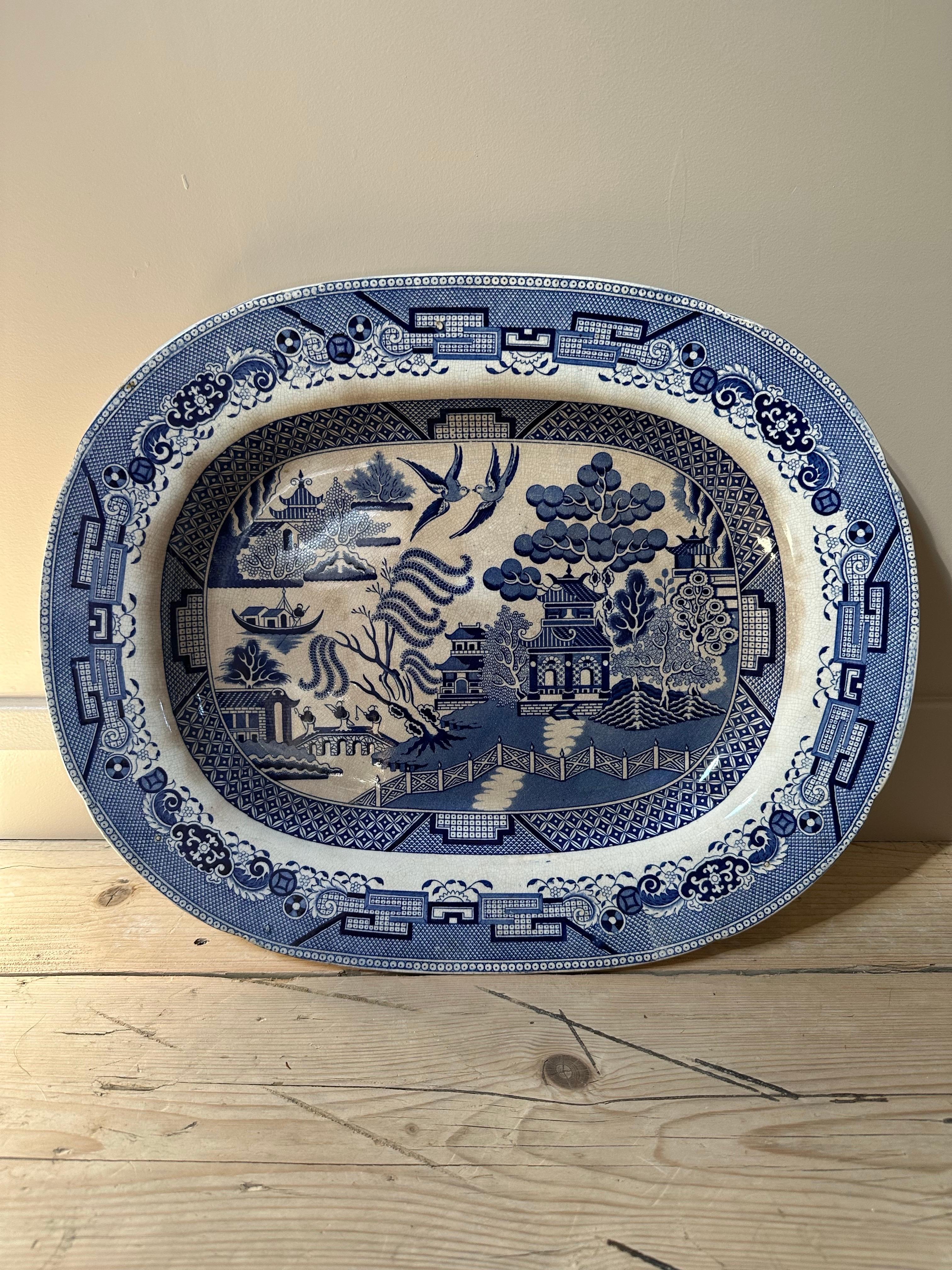 Ce grand plat de service exquis en céramique est orné du motif intemporel Blue Willow, un motif bien-aimé qui allie légende romantique et art classique. Datant des années 1850, cette pièce est un exemple étonnant de l'artisanat du XIXe siècle et de