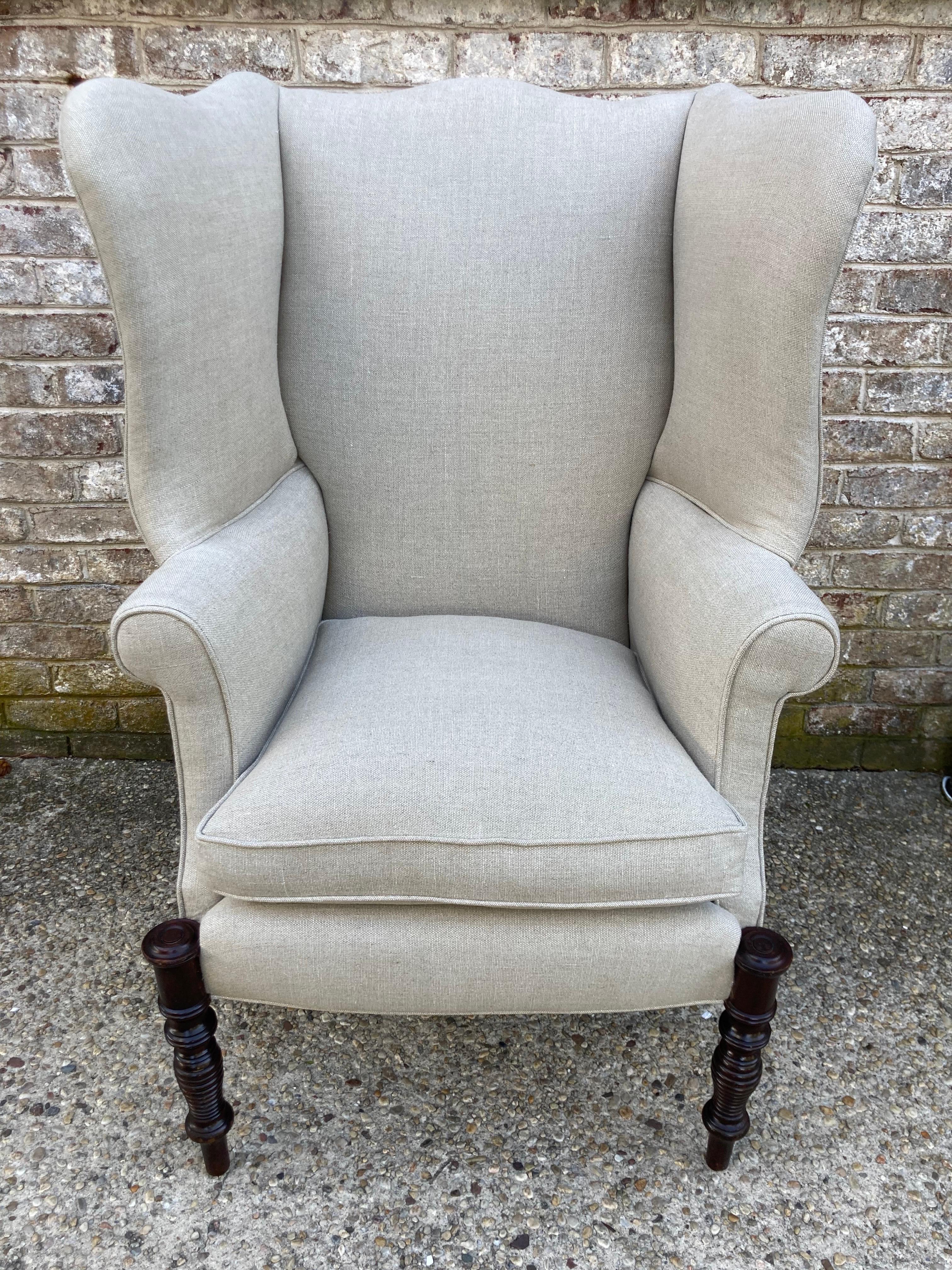 Antique Federal style wingback chair with interesting turned wood front legs. Newly reupholstered in natural linen with newly down wrapped seat cushion.