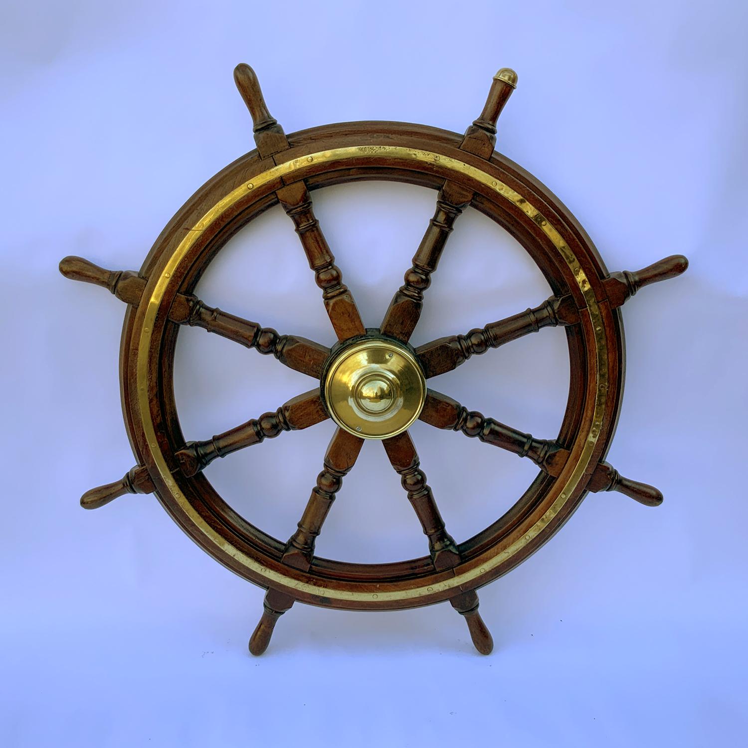 Eight spoke varnished wood ship's wheel with brass hub and brass trim ring. The brass hub cap is mounted to an iron hub. Warm patina on this maritime relic. Circa 1910. American made. Quite heavy.