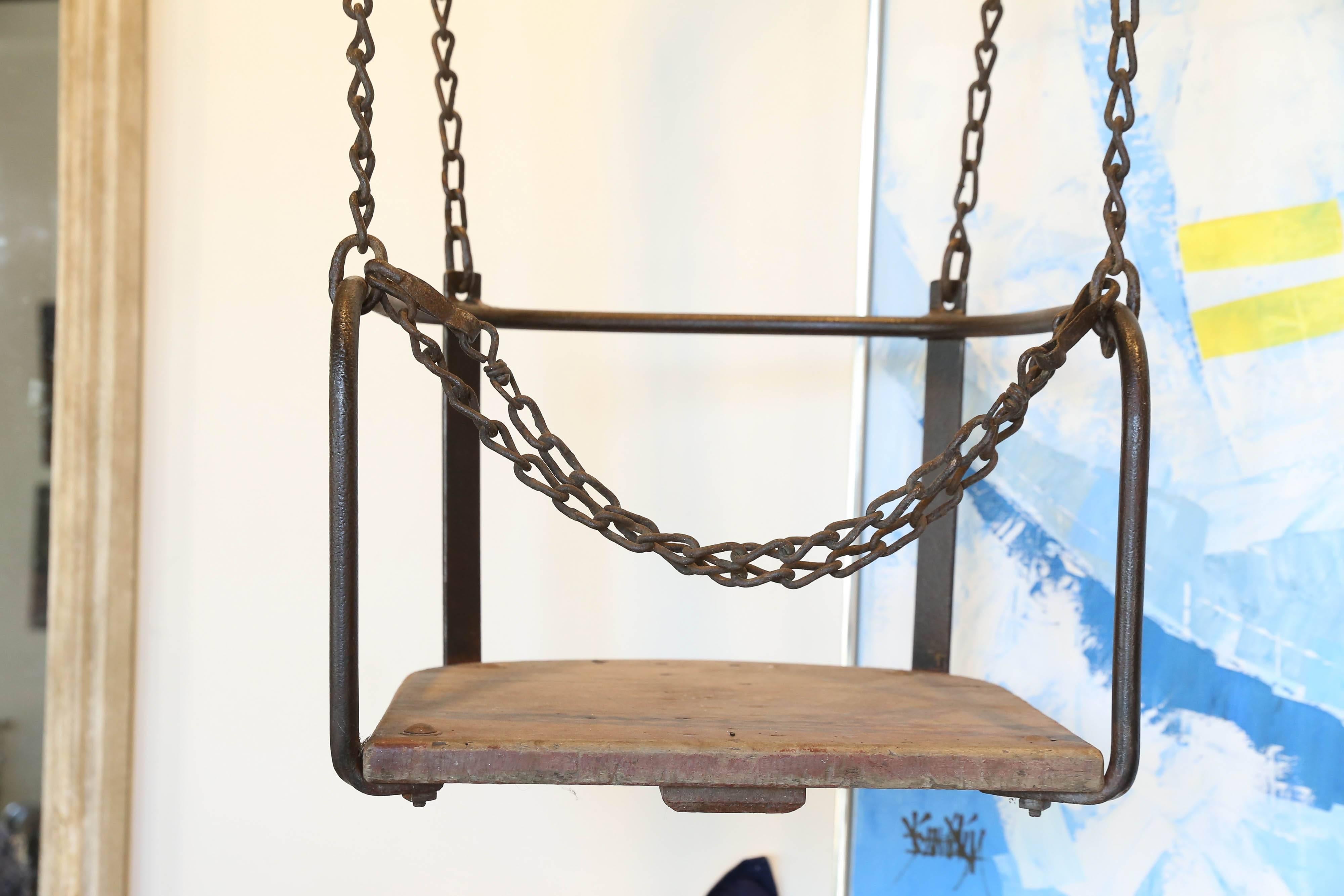 From France, a wood and metal swing suspended with forged iron chain from a heavy iron bracket. Most likely from a carnival ride, the seat is suspended 46 inches below the bracket and has a lap chain. The overall length of the piece is 67 inches.