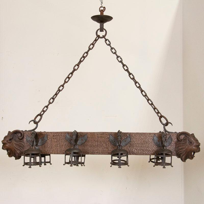 The hand carved, horned gargoyle faces on each end create drama in this oak chandelier from France. The horizontal shape makes it perfect for a long modern dining table, while the eight wrought iron 