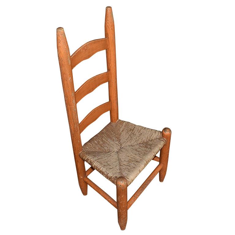 A children's American Arts and Crafts ladder back chair with a rush seat. We love a good ladder back chair, and this piece is perfect for a kid's room. Created from wood, the back features three ladders. Both the back and frame are painted orange.