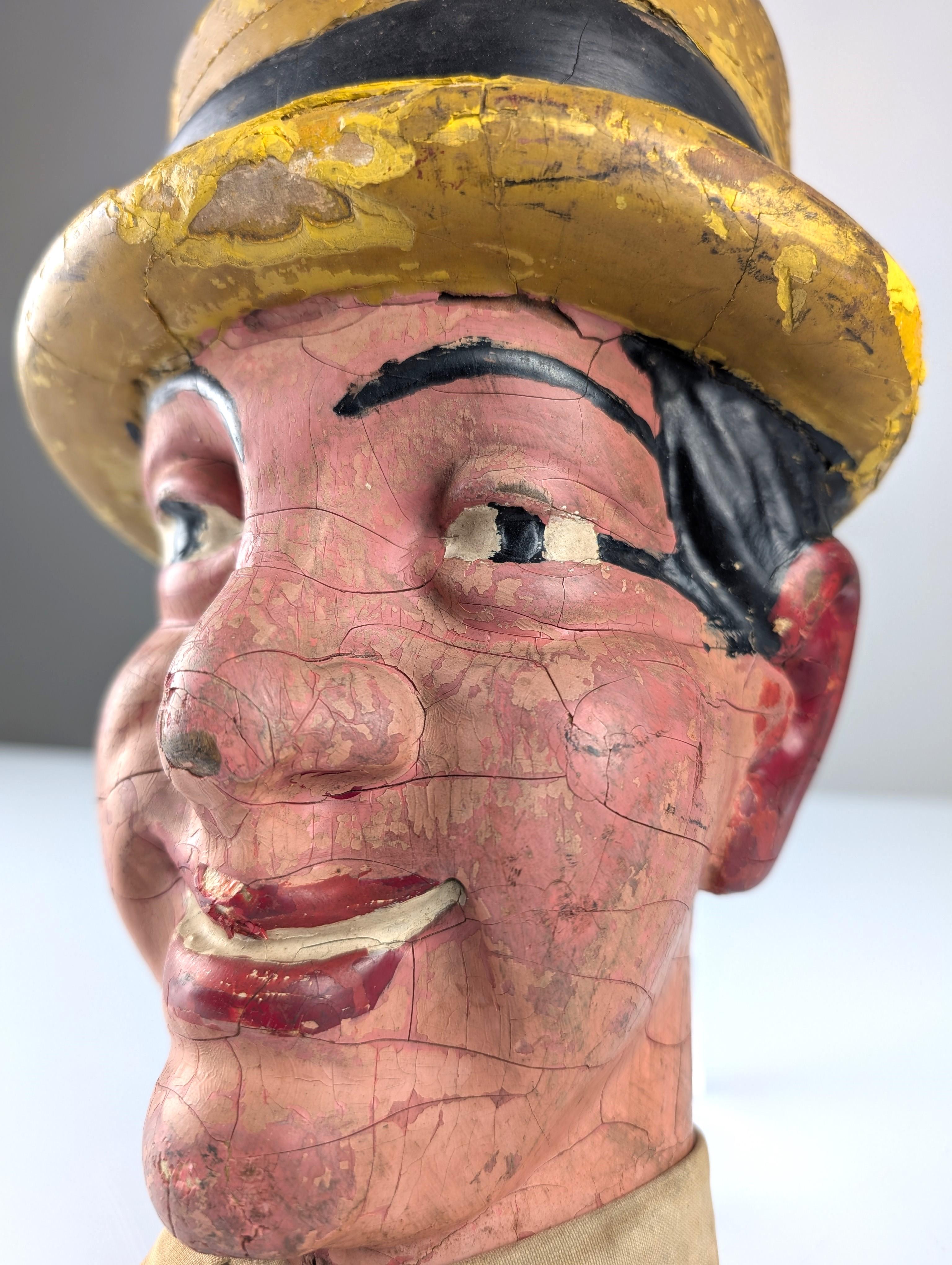 Antica testa in legno dipinta a mano, originariamente utilizzata come oggetto pubblicitario a metà del XX secolo, raffigurante l'iconico attore e cantante Martin. Con un sorriso espressivo, un caratteristico cappello giallo e un originale colletto