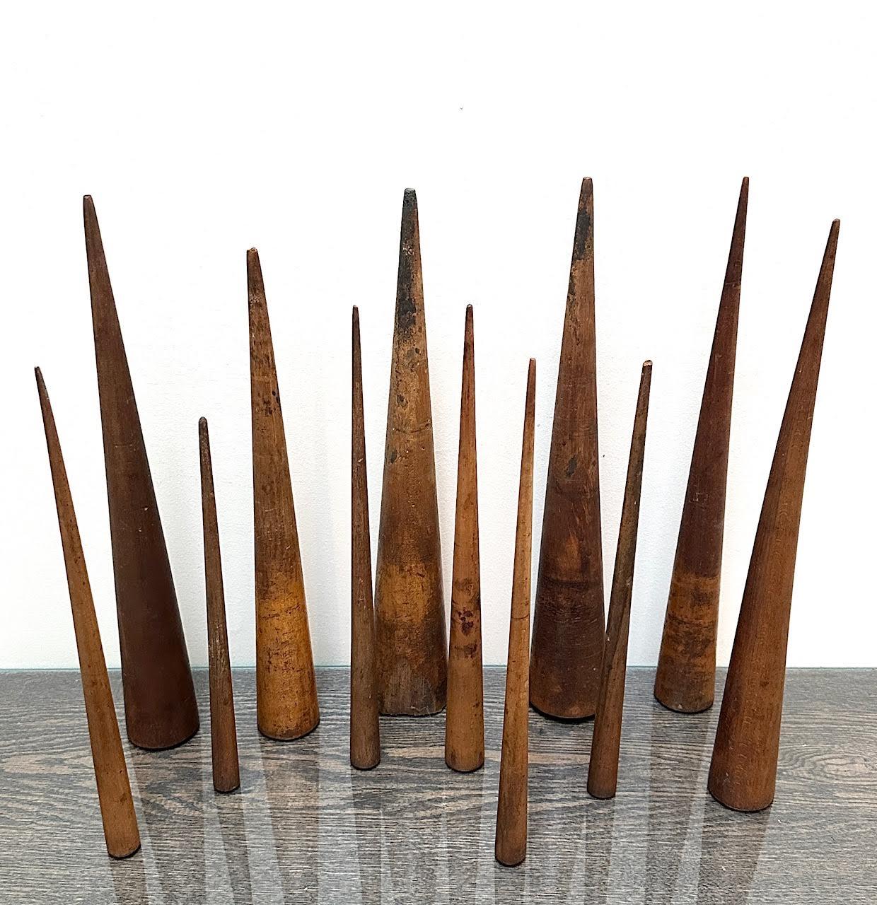 Una colección de 12 objetos antiguos de madera dura con forma de cono, de un tamaño que oscila entre 30 y 40 cm de alto. Posiblemente se utilicen como modelos arquitectónicos o herramientas de aprendizaje. Pueden disponerse en varias agrupaciones.
