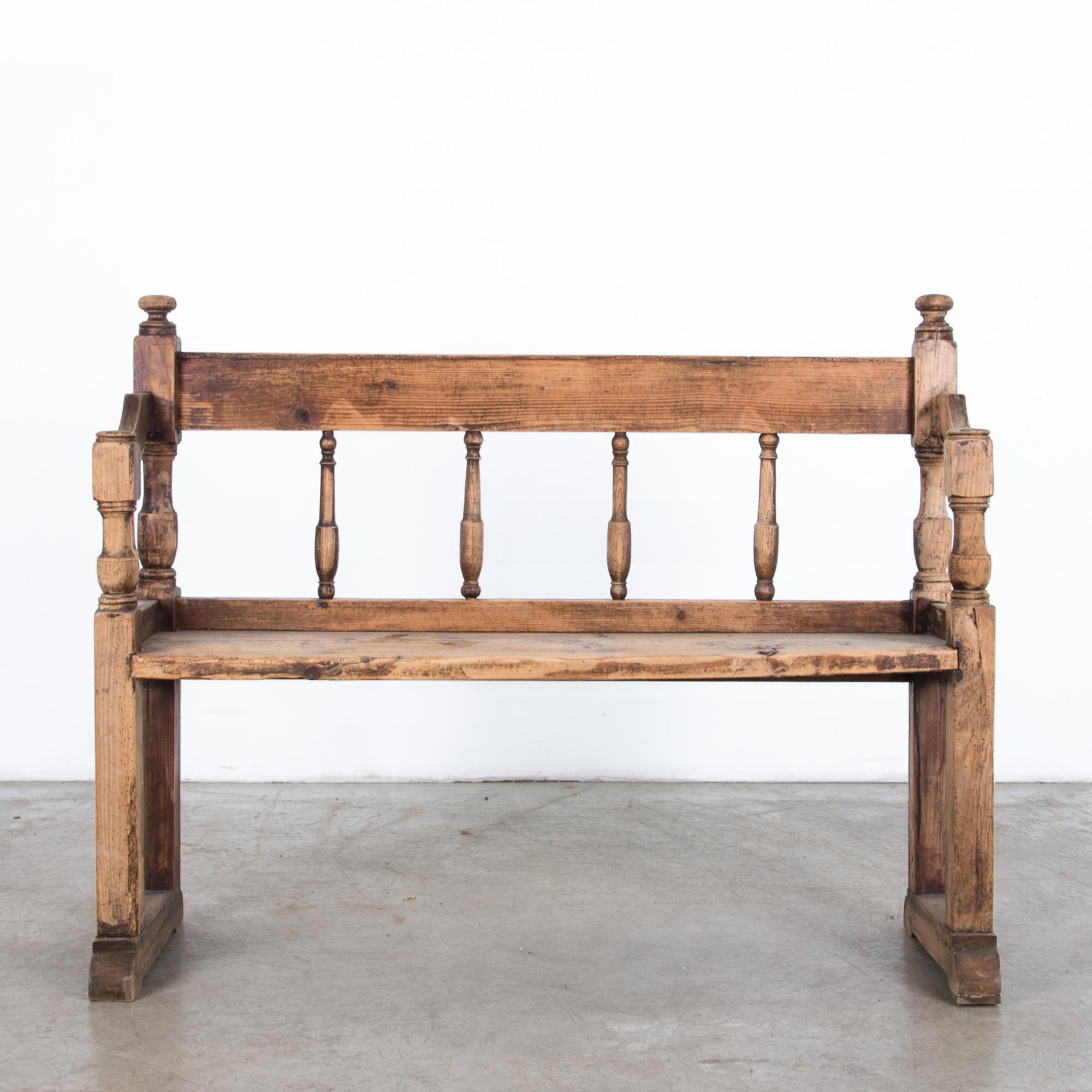 A wooden bench from France, circa 1900. Worn from years of use, a textured dark finish enhances the knotted and distressed wood for a charming high contrast patina. The traditional shape features turned wooden spindles and subtle carved details. A