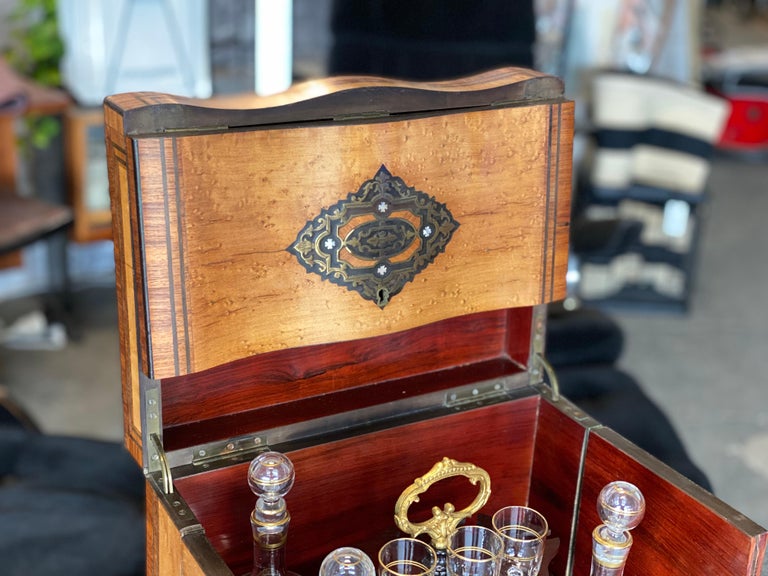 This is a beautiful boxed tantalus bar from the middle of the 19th century. The bar, also called a travel bar or advocate bar, is made of birdseye maple veneer and has ornaments of brass as well as mother-of-pearl inlays. It stands on cushion-like