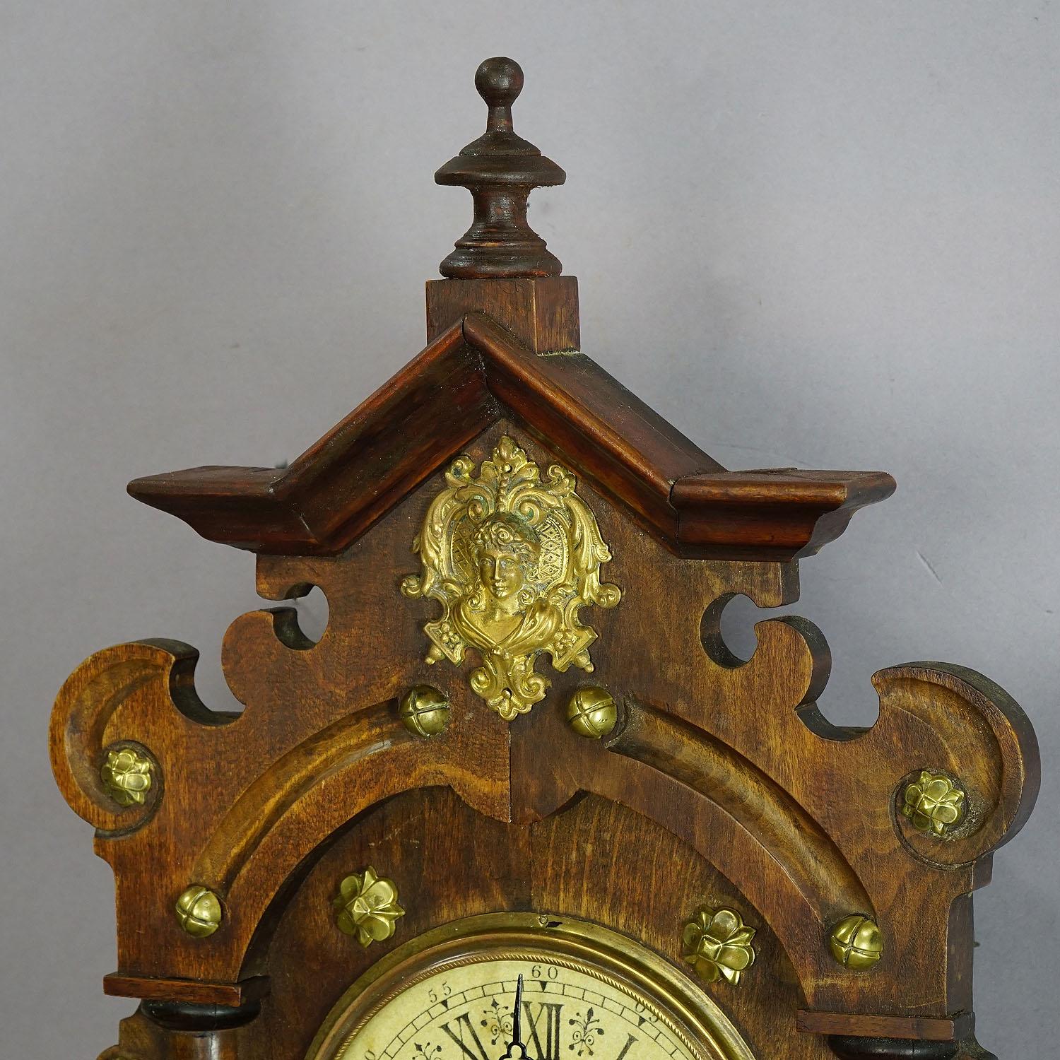 A lovely hand carved wooden wall clock decorated with several brass applications. Manufactured in Germany, circa 1920. Clockwork cleaned and overworked - in working order.

Measures: Width 9.25