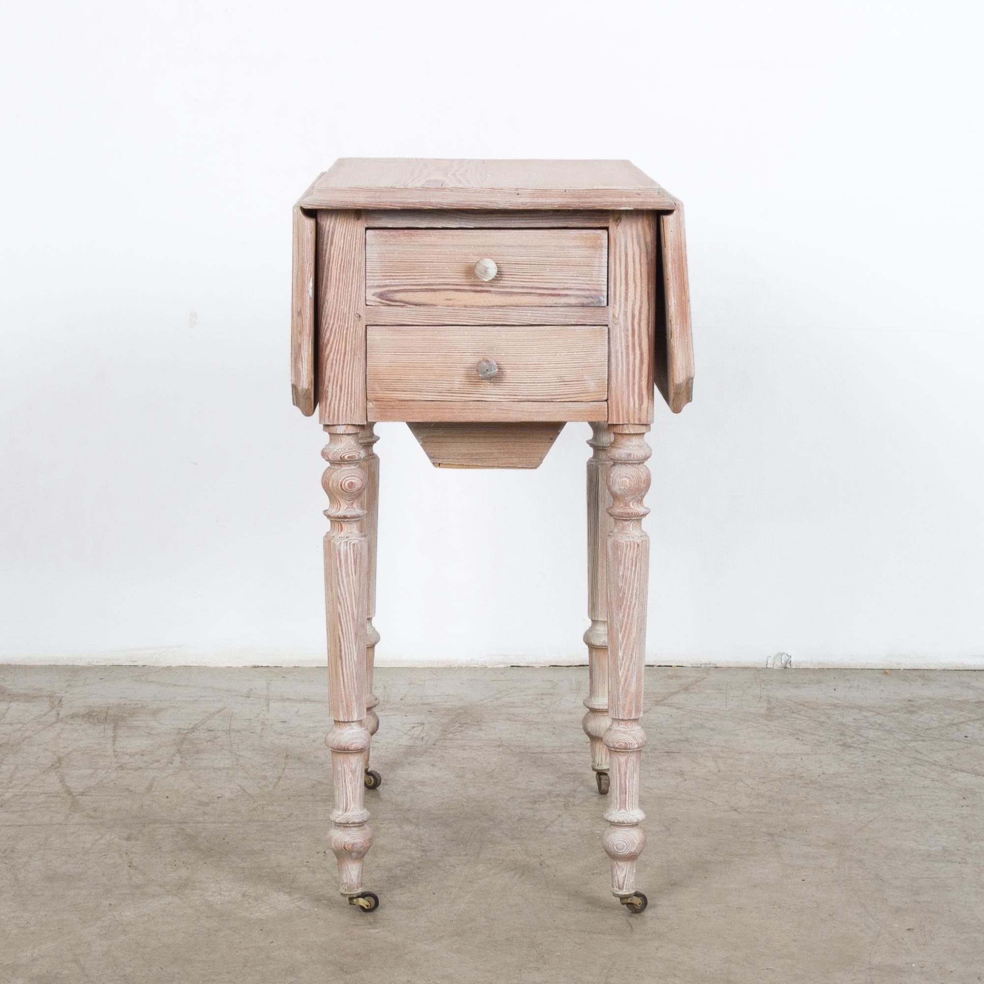 A wooden table from France, circa 1900. Two wings at the side can be folded out for a bigger table surface. The turned legs finish in small wheels, allowing the table to be moved with ease. Two lower pullout / pull-out drawers give a Classic