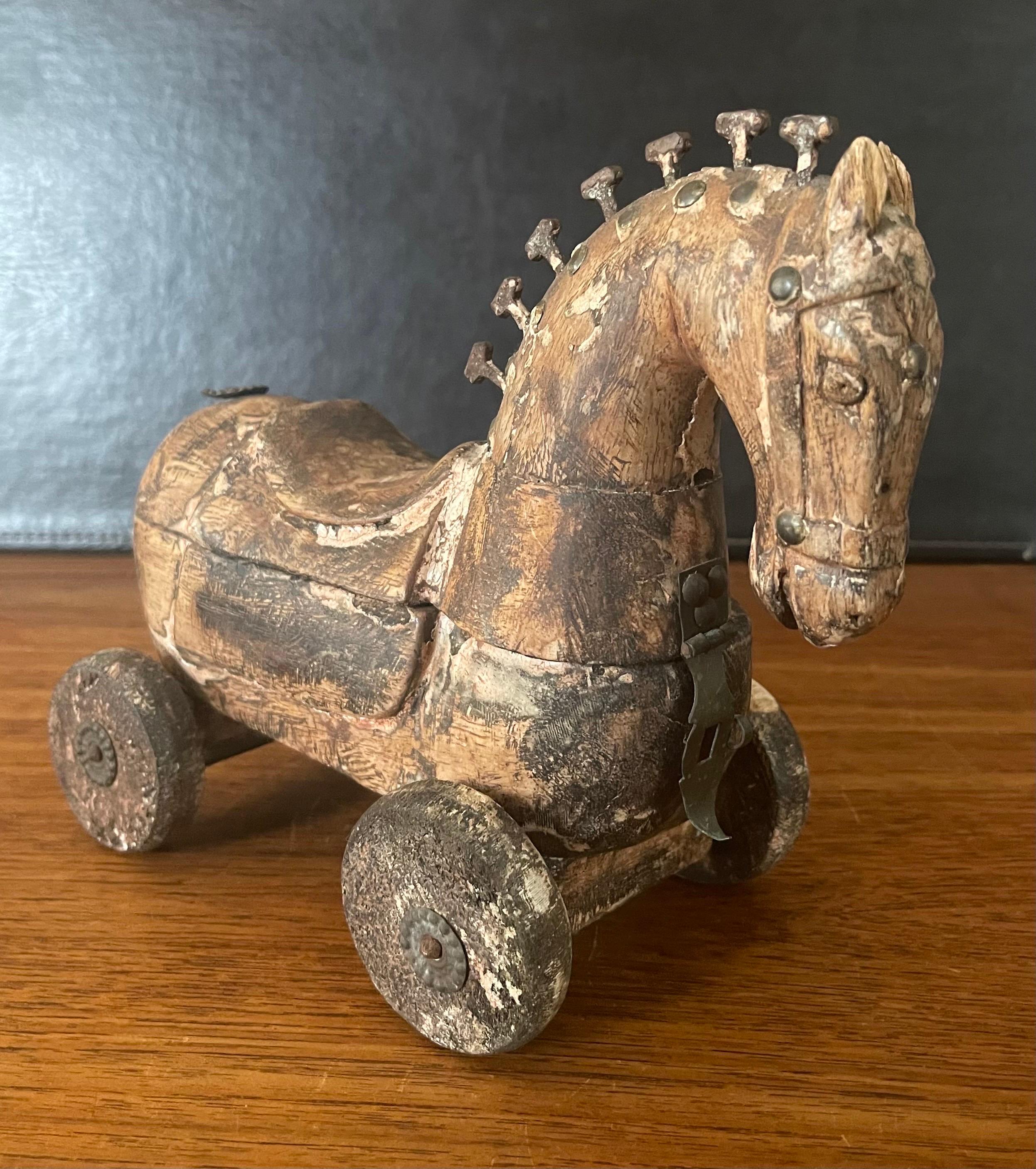 Antique wooden horse pull toy on wheels, circa 1930s. The piece has a latch in the front that allows you to rotate the top portion open to a hidden storage compartment. The horse is hand carved wood and the mane is made ot 