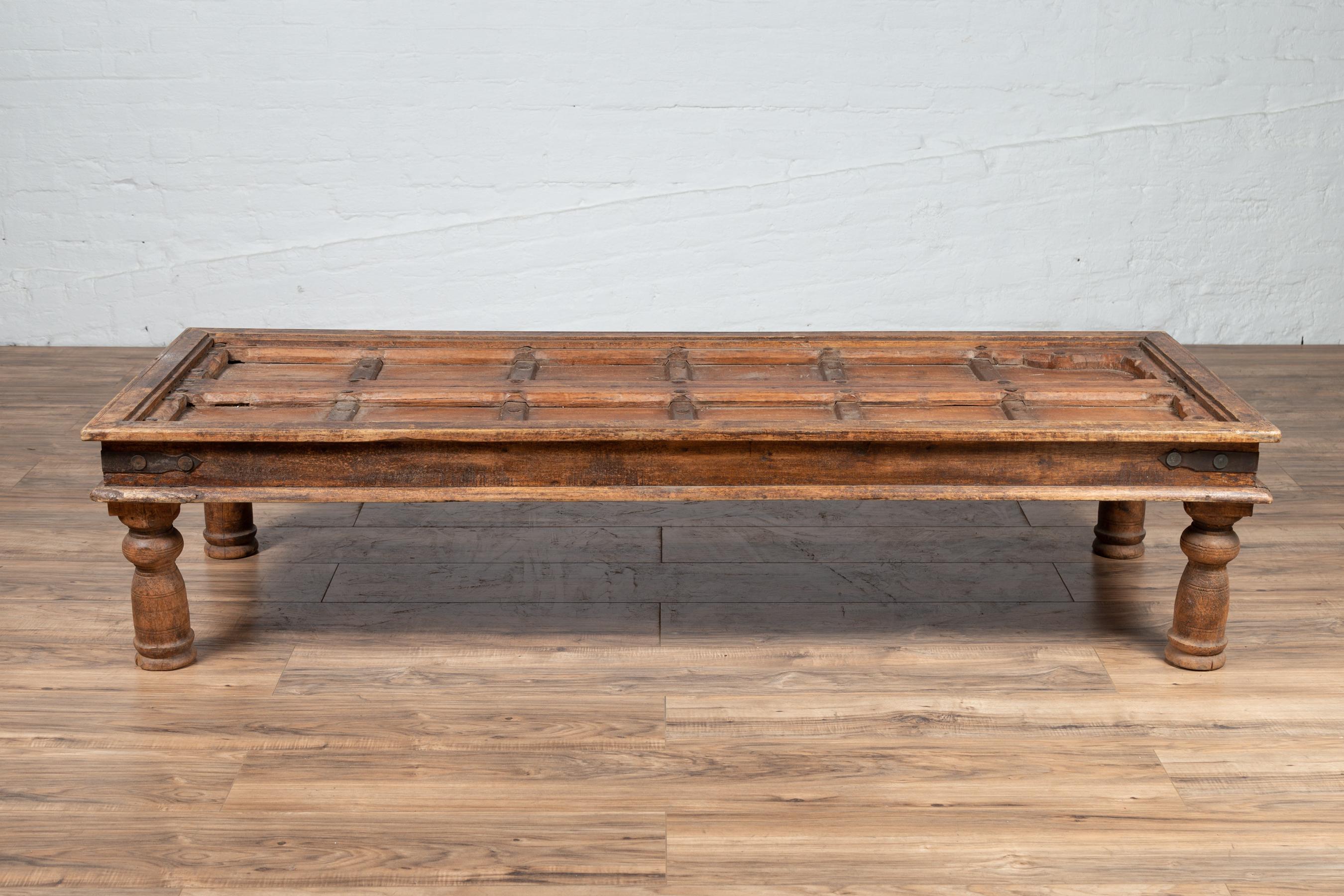 An antique Indian palace wooden door made into a coffee table with iron accents. Born in India during the early years of the 20th century, this exquisite palace door has been transformed into a coffee table. The top is rhythmically accented with