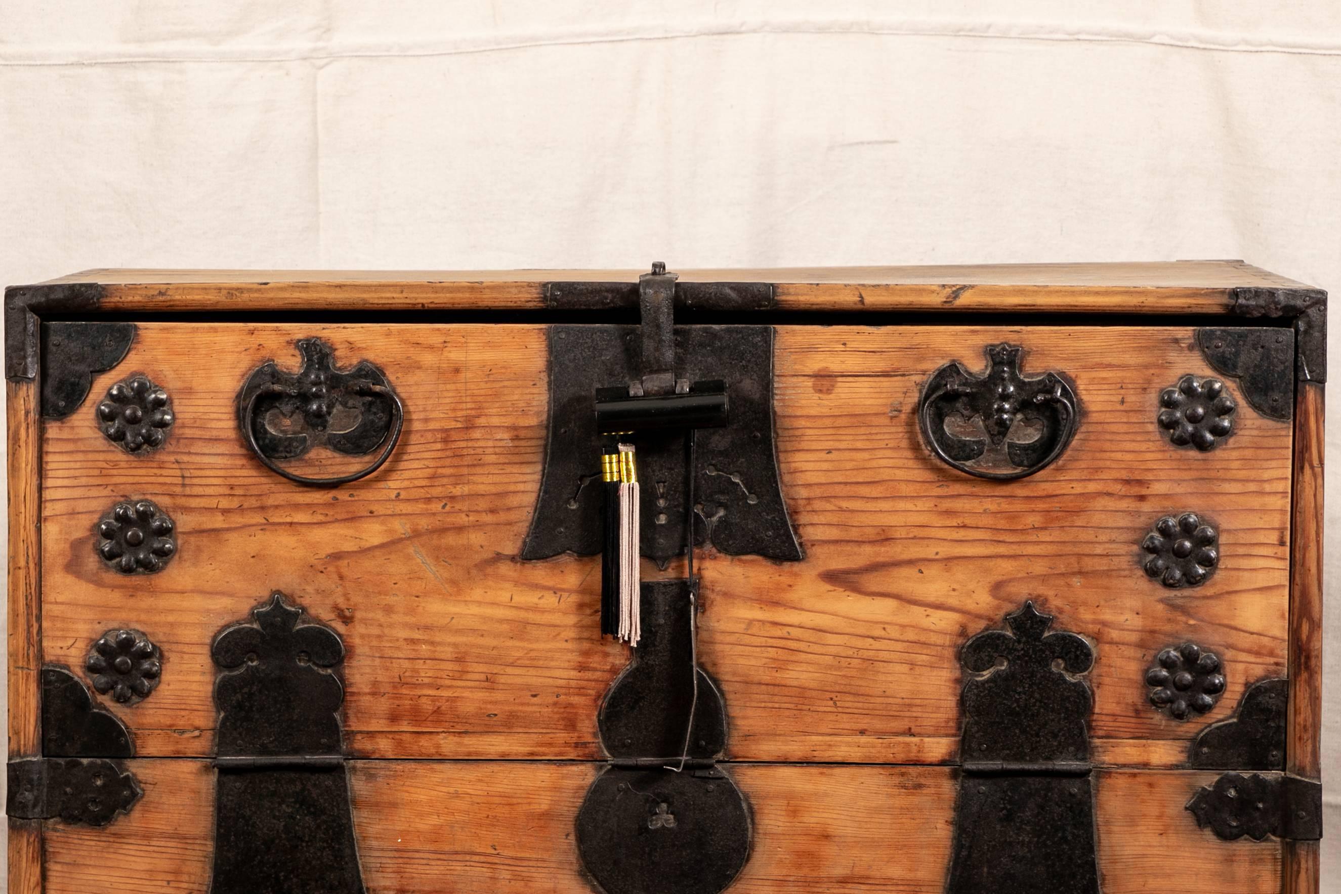 Antique wooden Korean chest, slant front opens to three short drawers with tab pulls over a deep storage compartment, decorative black painted iron hardware, hinges, pulls and a compartmental lock with carry handles on the sides. 

Condition: