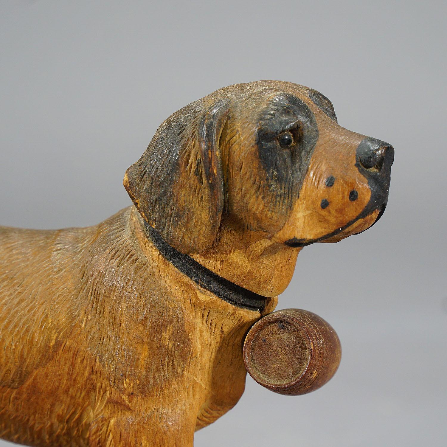 An antique early 20th century wooden carved sculpture featuring a St. Bernard dog with glass eyes. Handcarved in lindenwood and painted with naturalistic details. Manufactured in Swizerland in the area of Brienz, ca. 1930. Very good