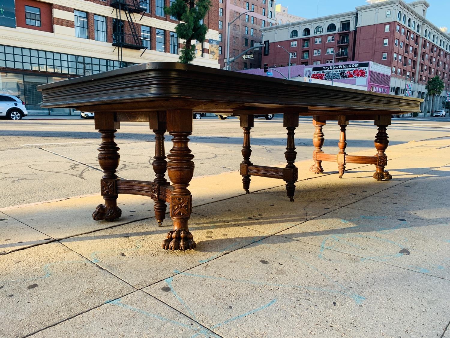 Stunning and beautiful antique dining table with 4 extension leaves and heavily carved wooden base.

The legs are very thick and heavily carved, the lion paw feet disguise the casters that make it easier to move since this table weights around 200