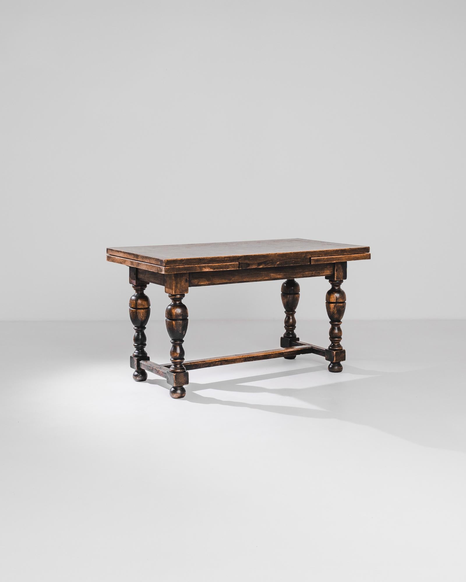 A Belgian wooden table with original patina, circa 1880. The folding tabletop, decorated by a solemn geometric ornamentation, transforms an intimate meal into a full-length dining table. Its sturdiness is accentuated by the laboriously carved