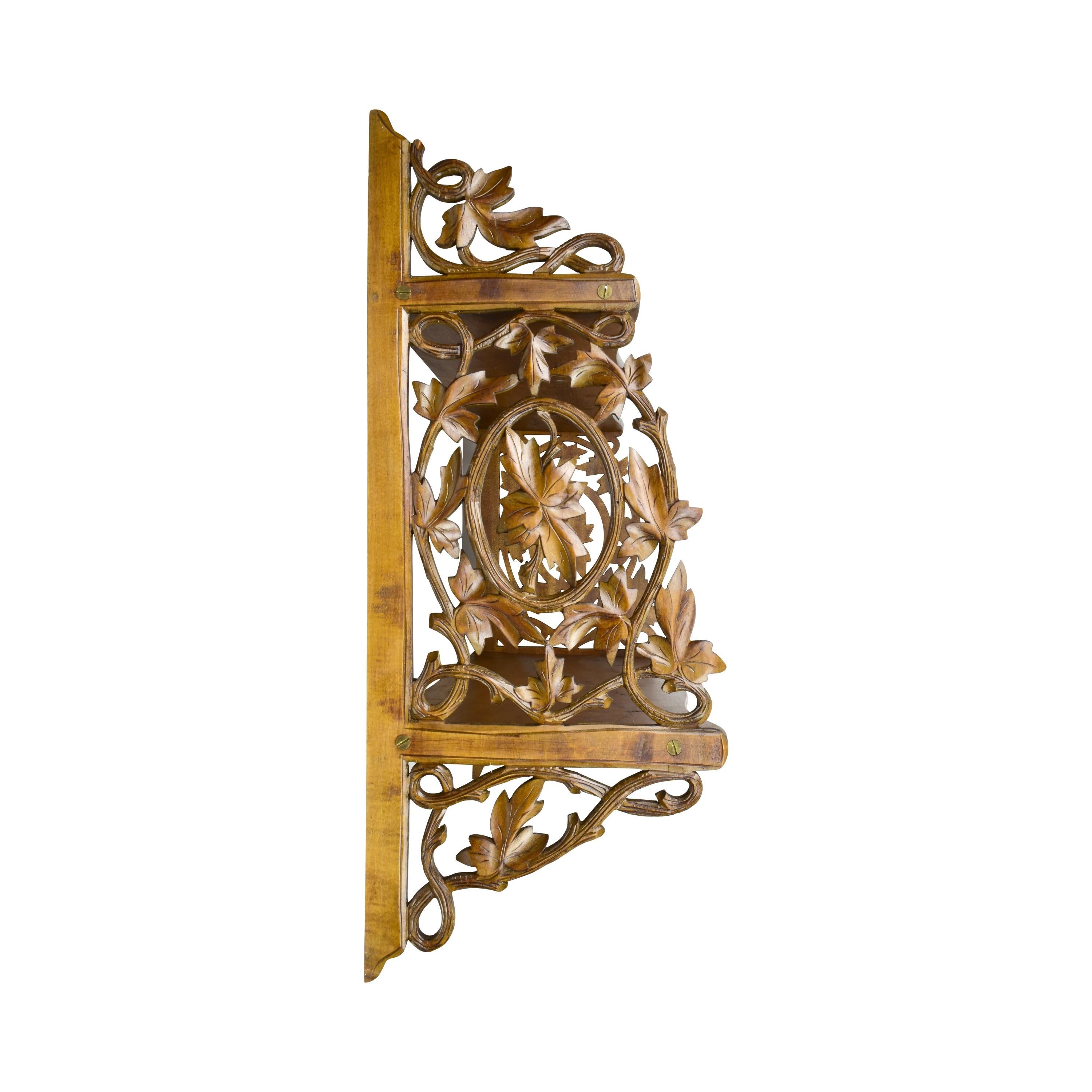 Esta exquisita estantería de pared de madera antigua presenta intrincadas tallas de hojas y zarcillos de vid, mostrando una artesanía excepcional típica de la región de Brienz o Selva Negra. Los soportes laterales decorativos están adornados con