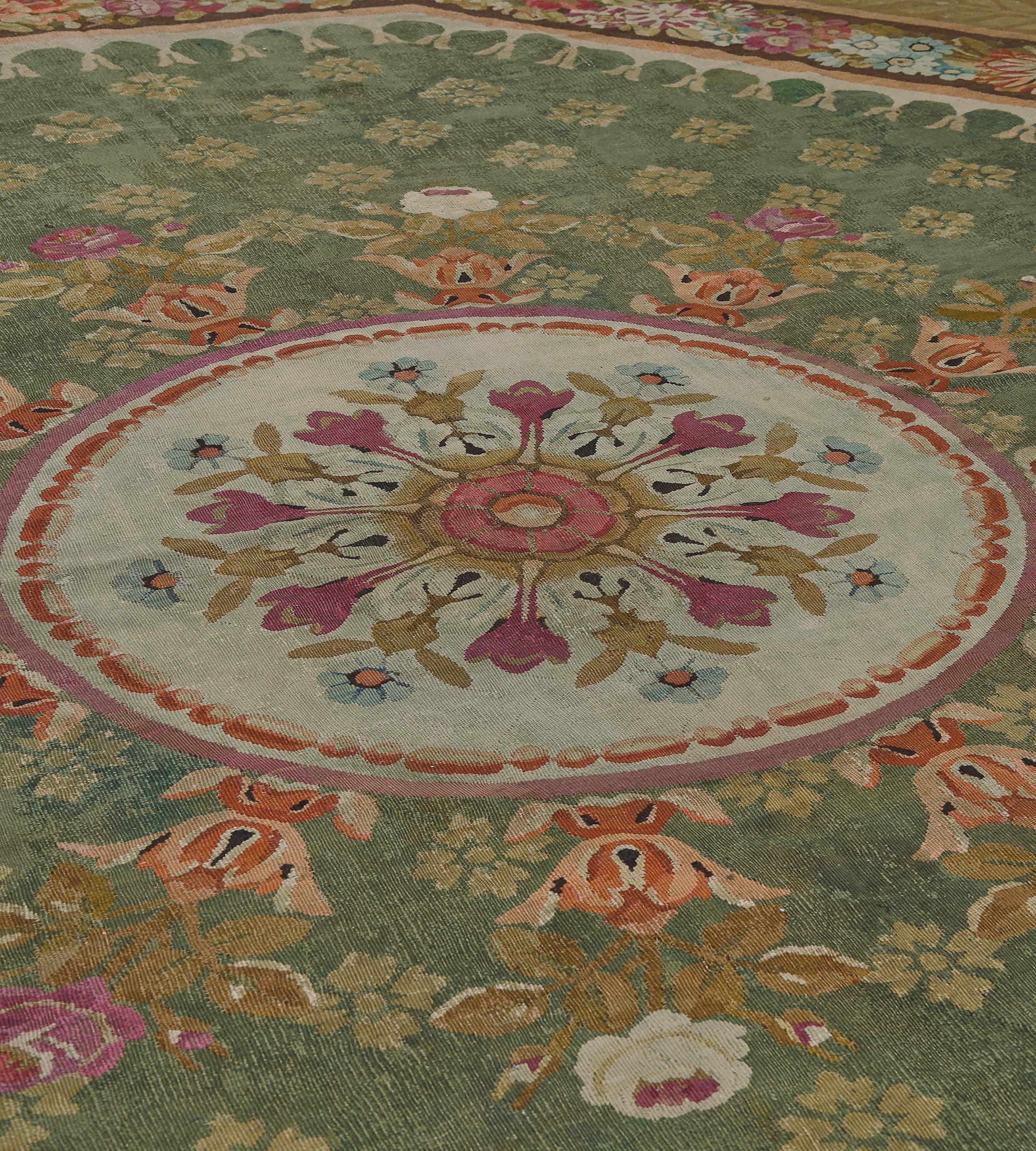 This antique French Aubusson rug features a moss-green field surrounded by an octagonal ivory stripe with an ivory inward hanging tassel and scattered with pistachio-green flowerheads around a central ivory roundel containing a large rosette issuing