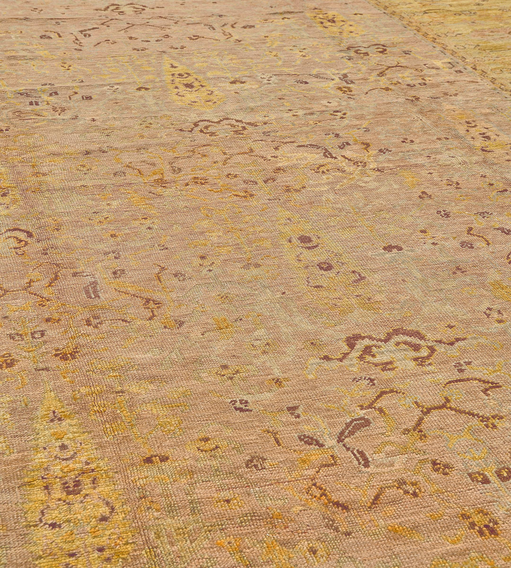 Questo antico tappeto Oushak presenta un campo di terracotta chiara con una palmetta e una vite floreale di colore giallo oro e rosso bordeaux, in un ampio bordo giallo oro con delicate palmette e viti floreali tra strisce di viti floreali
