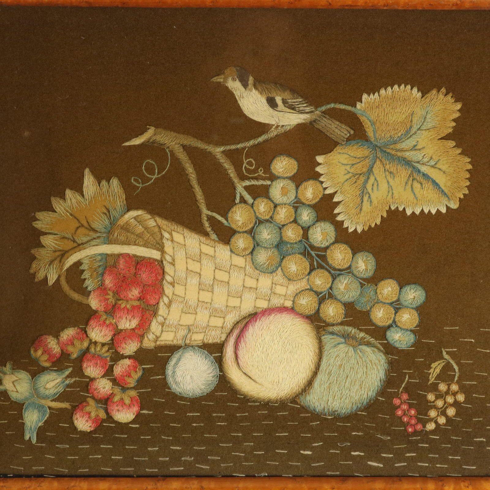 Georgian woolwork on felt, bird with fruit basket embroidery. The embroidery is worked in fine wools on a brown felt-like ground, in a variety of stitches. Colours red, blue, brown, beige and green. Scene depicts strawberries pouring out of a basket