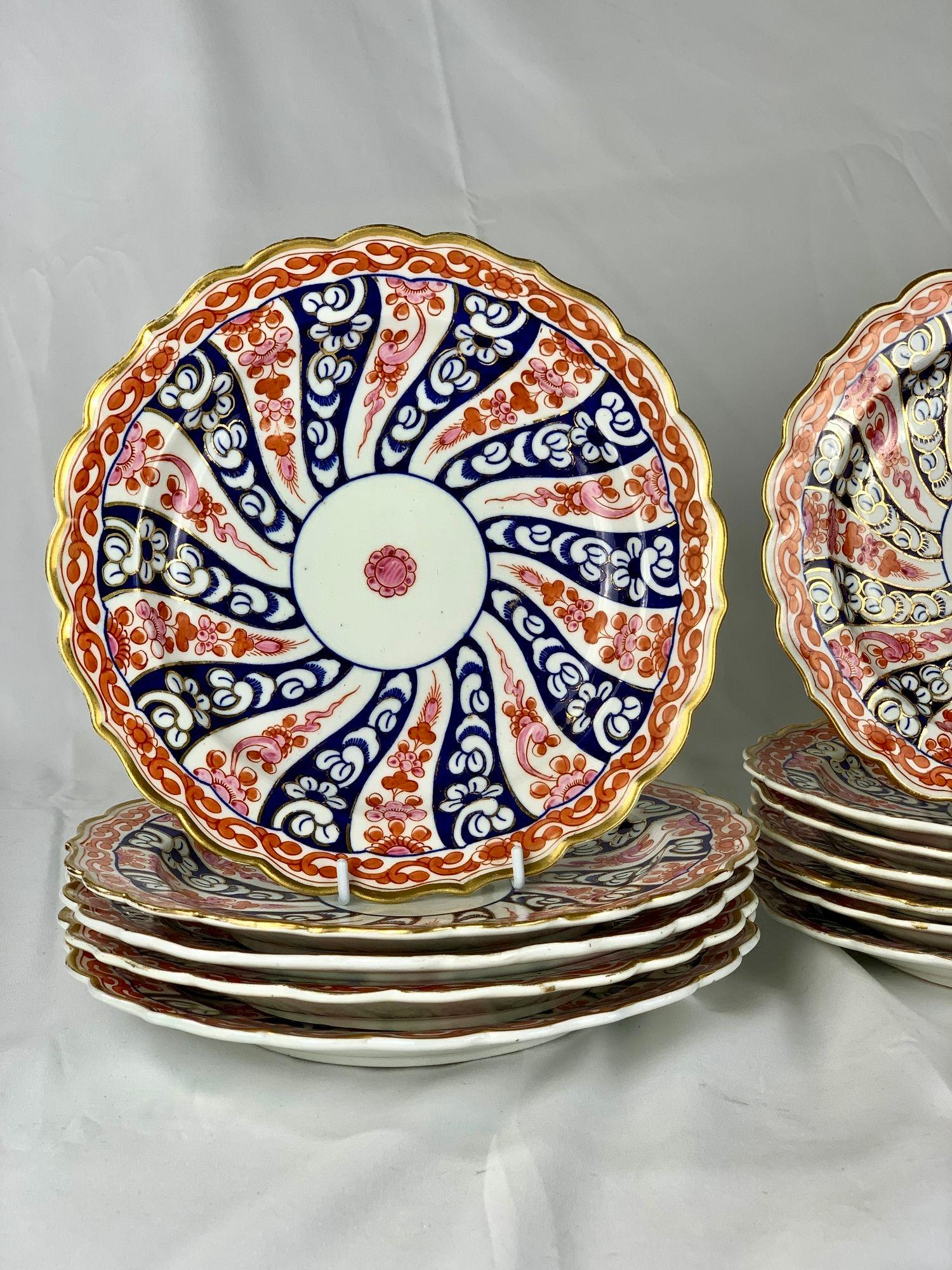 El motivo de la reina Carlota en estos platos de porcelana Worcester presenta un llamativo diseño de remolino radial con secciones alternas de azul cobalto y rojo hierro. Las intrincadas volutas blancas y los motivos florales añaden refinamiento al