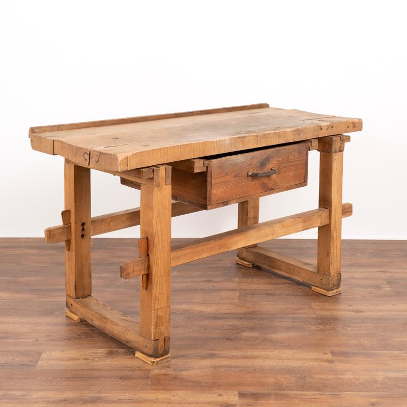 This rustic table served as a work table for generations of use, seen in the heavy distress, gouges and darker patina along the top. A large metal 