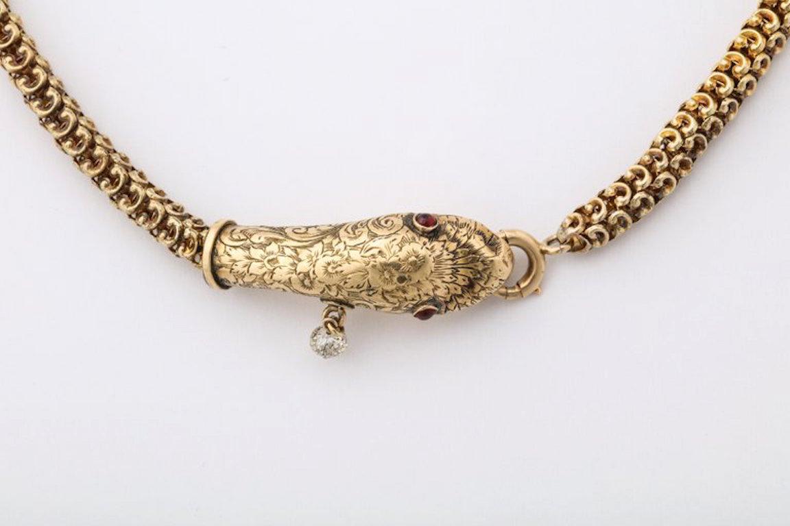 An exceptional antique snake necklace with 14 karat gold box chain body chased decorated head and ruby eyes and diamond dangling from it's mouth.
