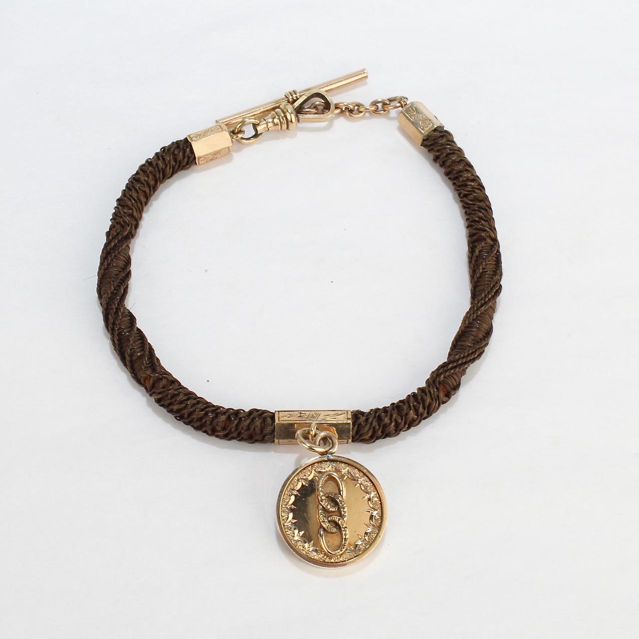 An antique Victorian memorial watch chain of woven hair.

Mounted with gold-filled findings and set with a gold-filled medallion that likely is an Odd Fellows fraternal coin.

The coin itself has a cityscape scene with a castle on one side and 3