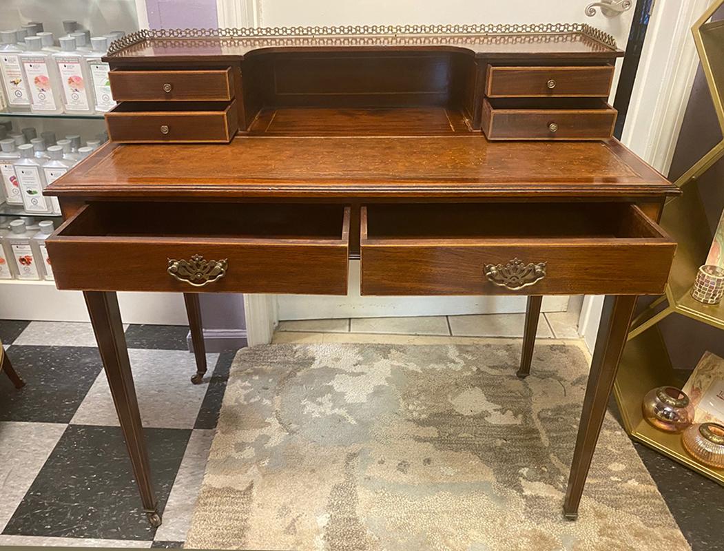 Beautiful antique writing desk or vanity. Original leather top has been restored to its original glory. The gallery with brass open work adorns the three sides. The gallery is not removable. The brass hardware and casters are original. Solid