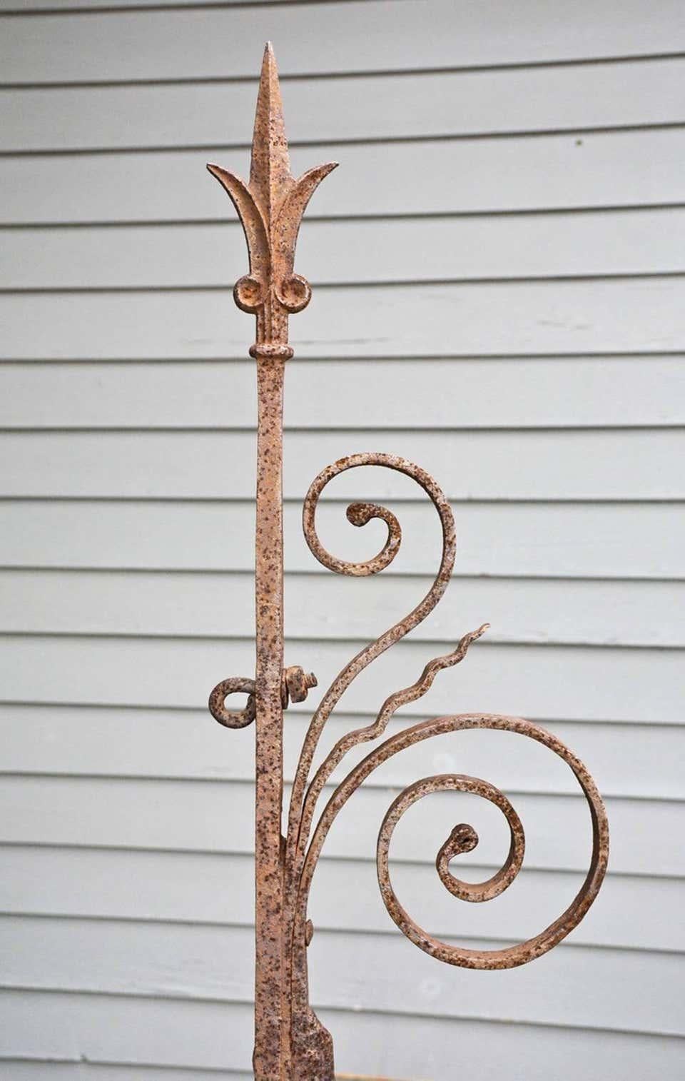 The antique wrought iron bracket is decorated with curls and a spear-like tip. Holes on the side bar can be used to secure to the side of a building. Sign can be attached to the horizontal bar for display.