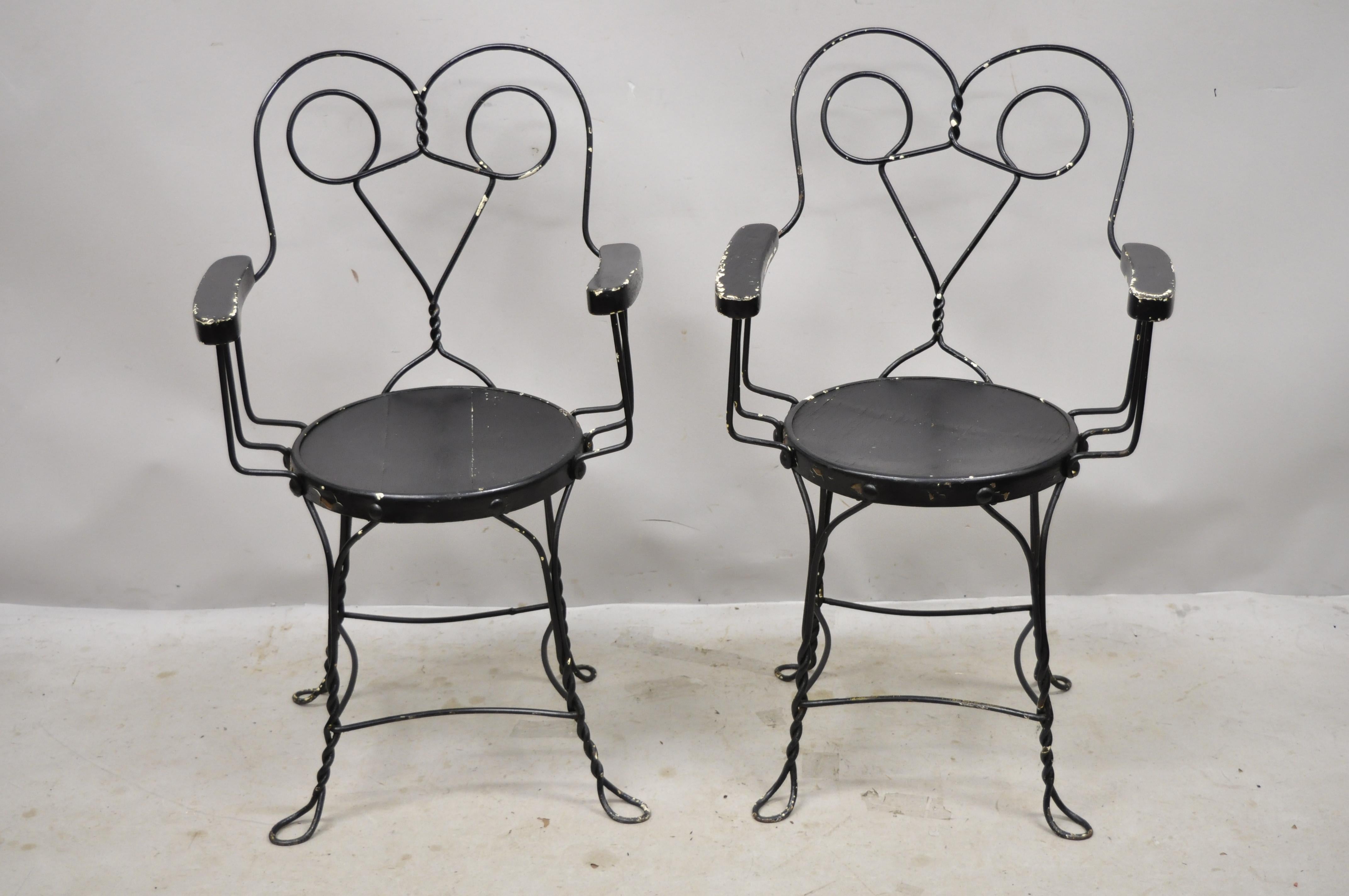 Antique wrought iron twisted metal ice cream parlor arm chairs with wood arms - pair B. Item features wooden armrests, wooden round seat, twisted metal frame, metal frames, very nice antique pair. Circa Early 1900s. Measurements: 35