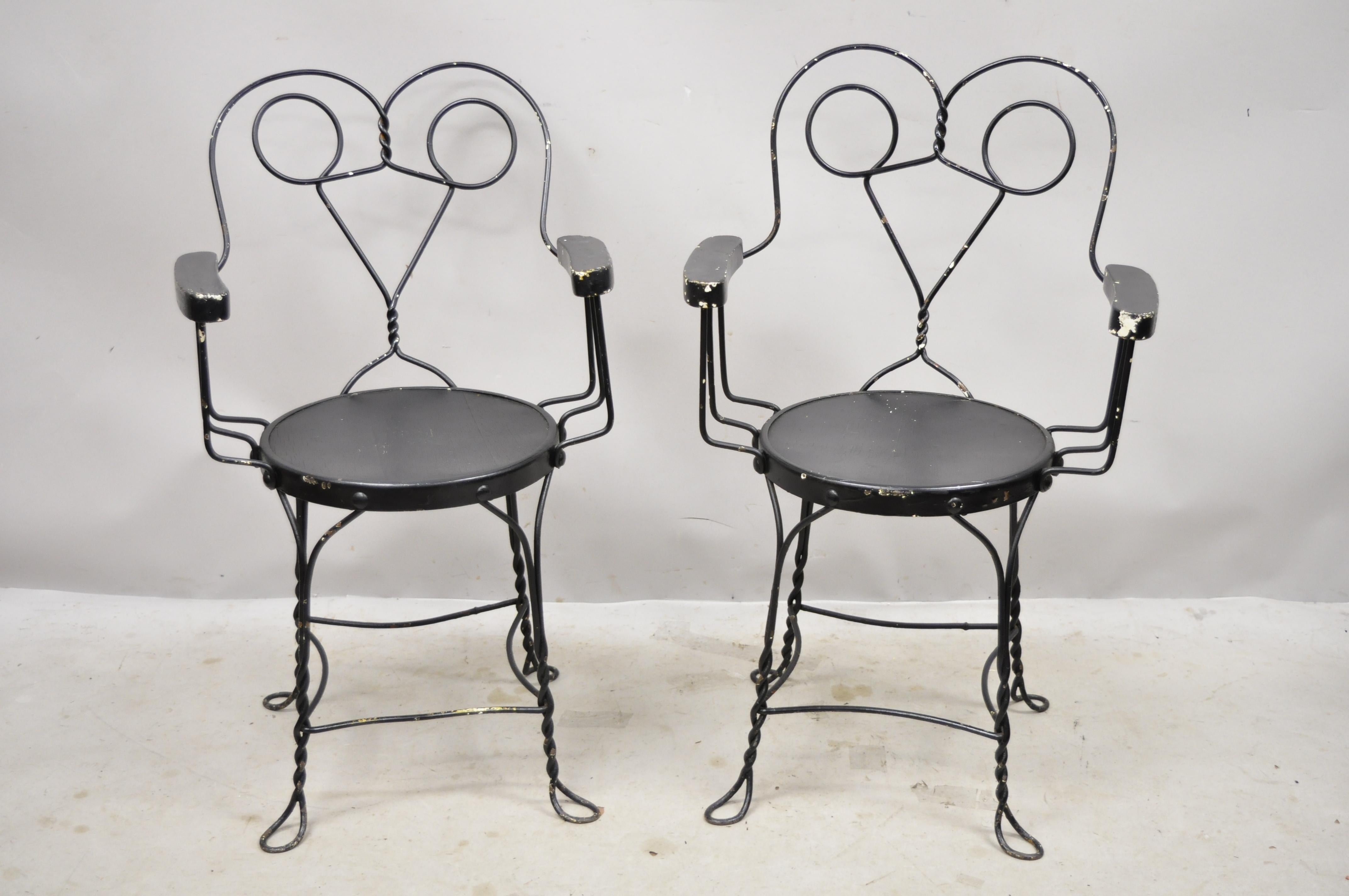 Antique wrought iron twisted metal ice cream parlor arm chairs with wood arms, pair A. Item features wooden armrests, wooden round seat, twisted metal frame, metal frames, very nice antique pair, Circa early 1900s. Measurements: 35