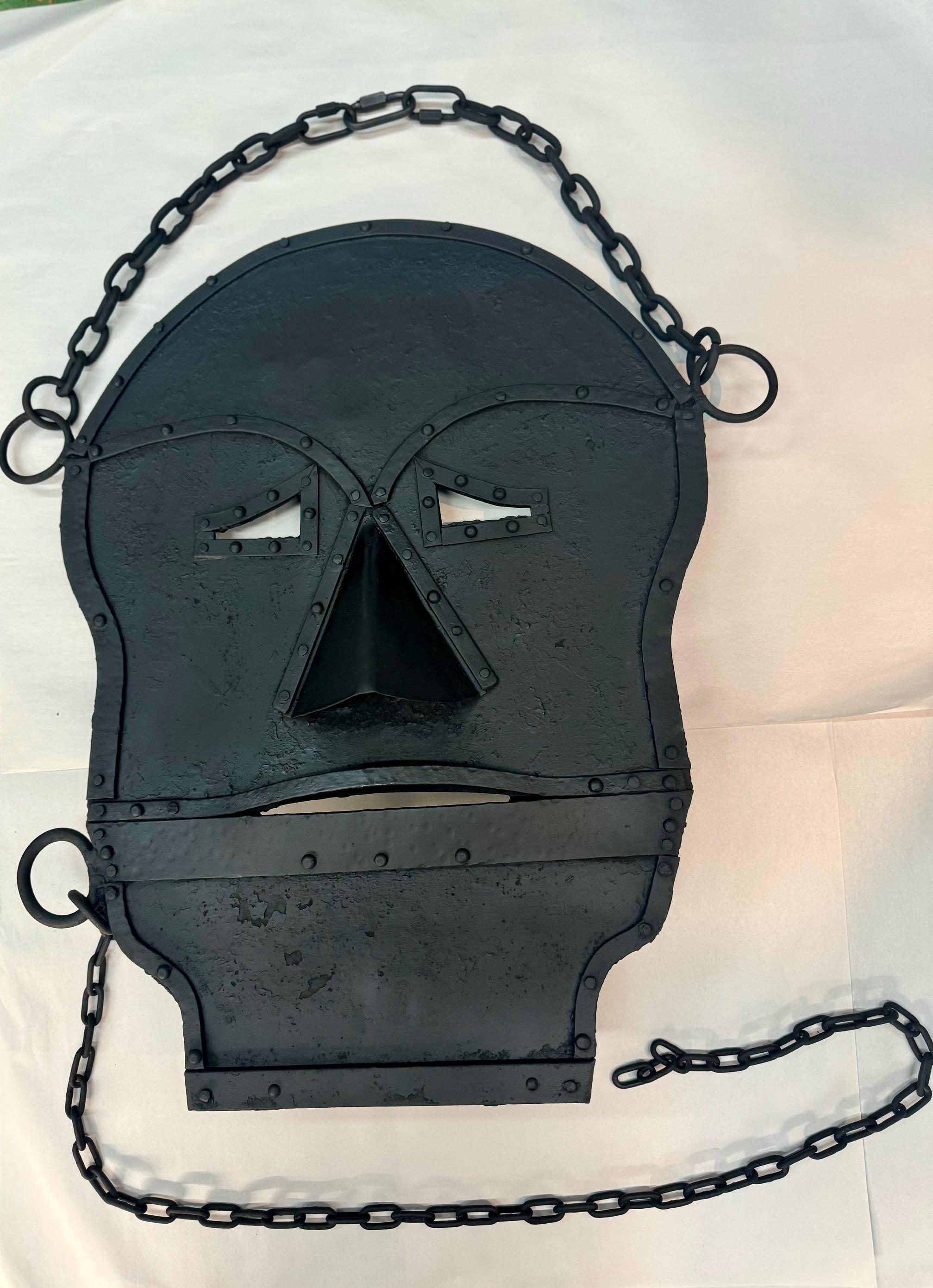 Este gran cartel de máscara de soldador de doble cara colgaba fuera de una ferretería  taller audazmente visible para el que viene y el que va. Sostenida por pesadas cadenas, la señal de la máscara era espeluznante y un poco siniestra, y no apta