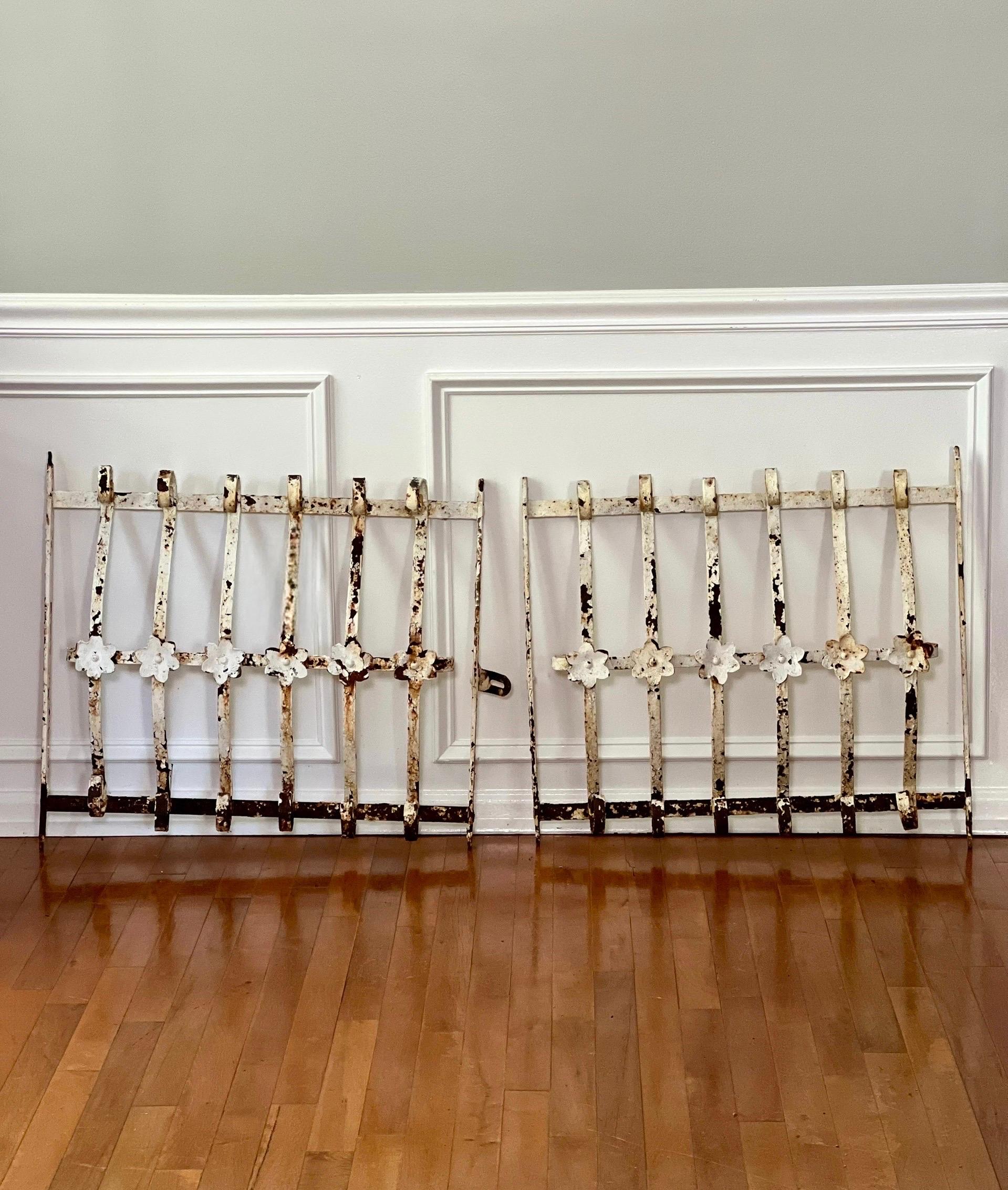 Charming pair of 19th century wrought iron window grills.  The pair served as a gate for decorative and security purposes with one having a hasp.  Each one has bowed scroll work adding depth and dimension to their beauty with floral detail.  They