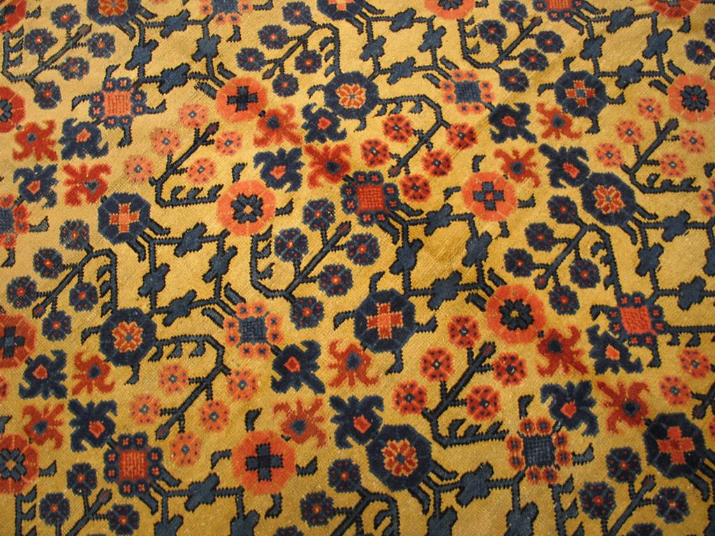 Rarely are East Turkestan carpets square. An allover repeat pastern of formal flower sprays neatly occupies the straw yellow field of this late 19th century rug. The main border is the Chinese rainbow wave, but the inner rams horn hook stripe and
