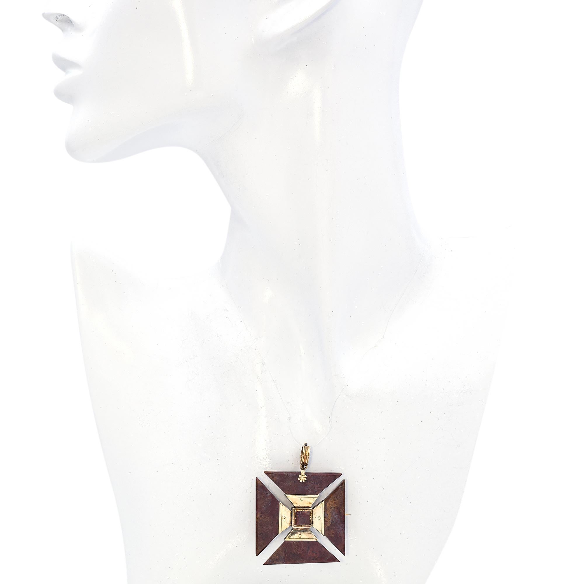 Cette broche étonnante présente un motif géométrique audacieux. La pièce maîtresse est une pierre de jaspe brun, sertie dans un cadre carré. Quatre segments triangulaires rayonnent vers l'extérieur, chacun mettant en valeur la texture et la couleur