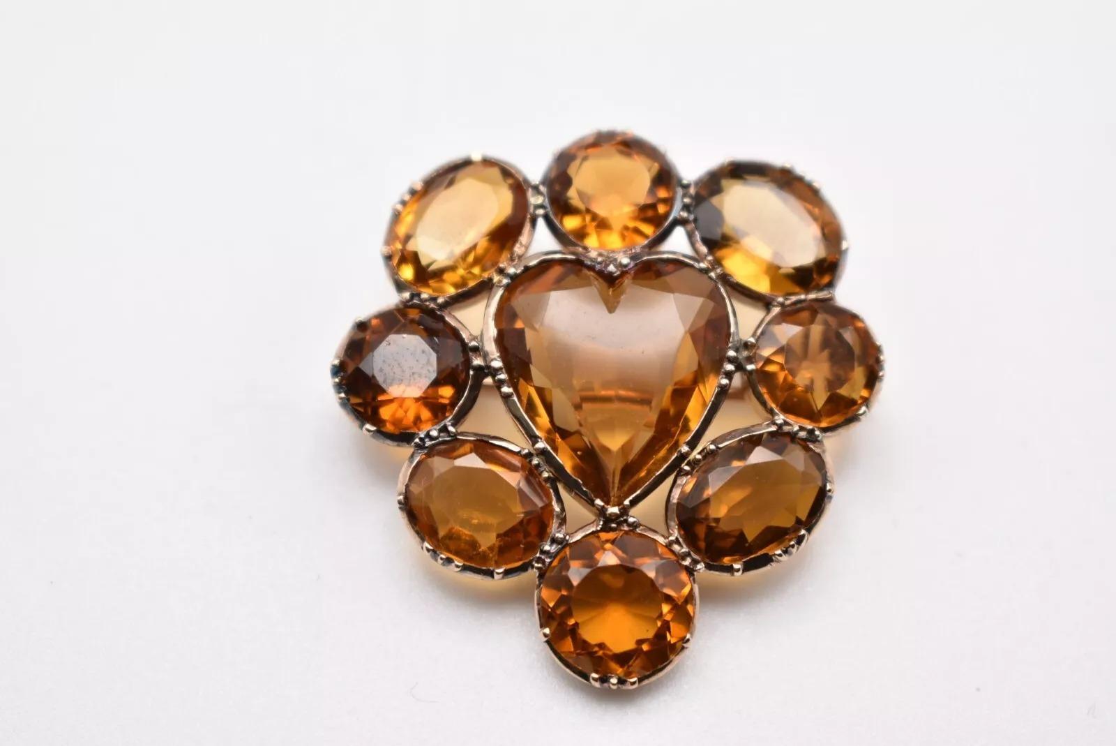 This exquisite antique brooch, dating back to the first quarter of the 20th century, showcases a beautiful design crafted from unmarked yellow gold, assessed as 9ct. The centerpiece of this elegant piece is a heart-shaped golden citrine, measuring
