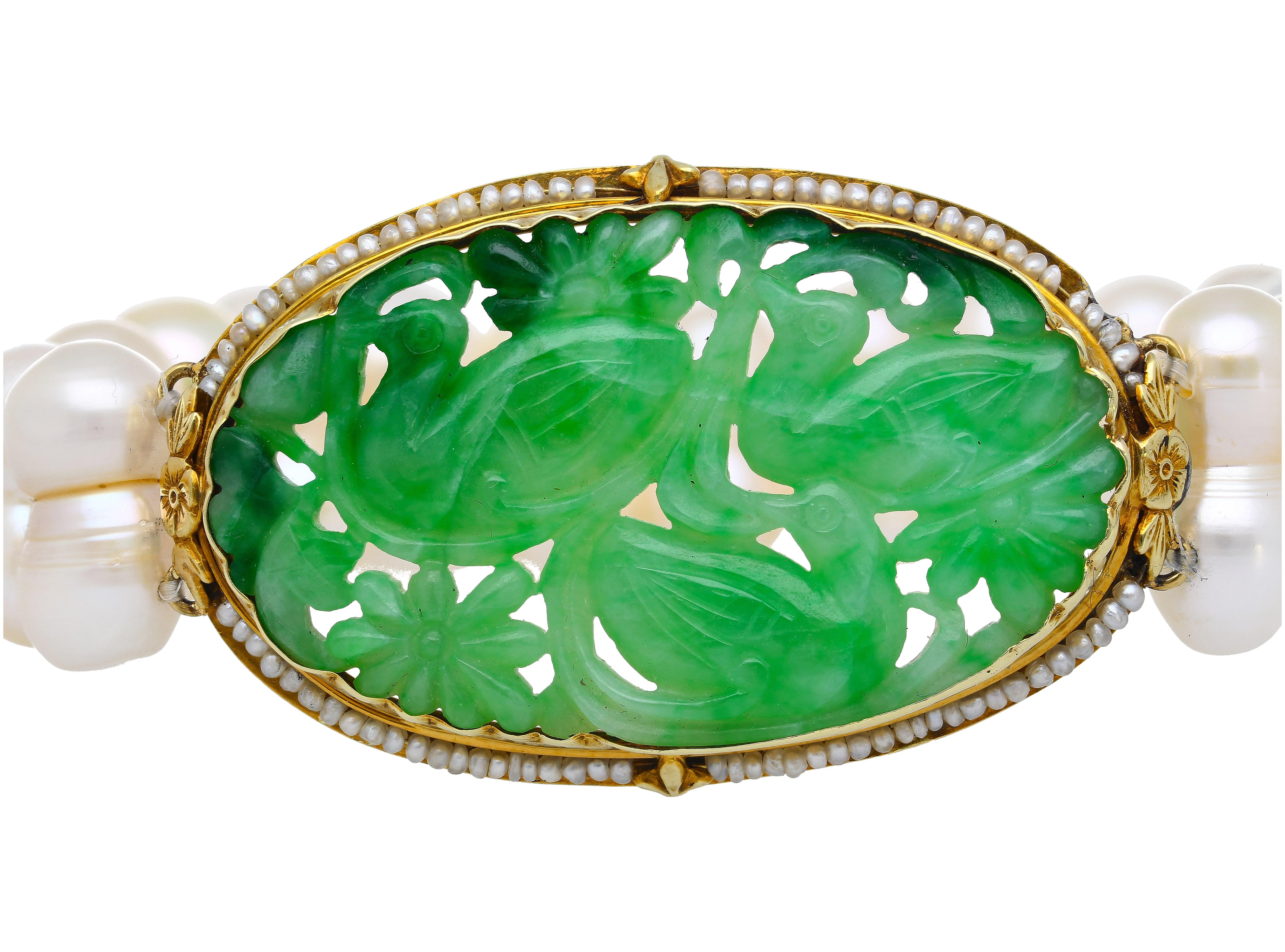 This antique piece features a stunning carved jade piece depicting a pigeon and flower motif. The Jade is encircled by yellow gold and and the band of the ring is made up of two strings of natural grade A pearls. 

This antique ring originated from