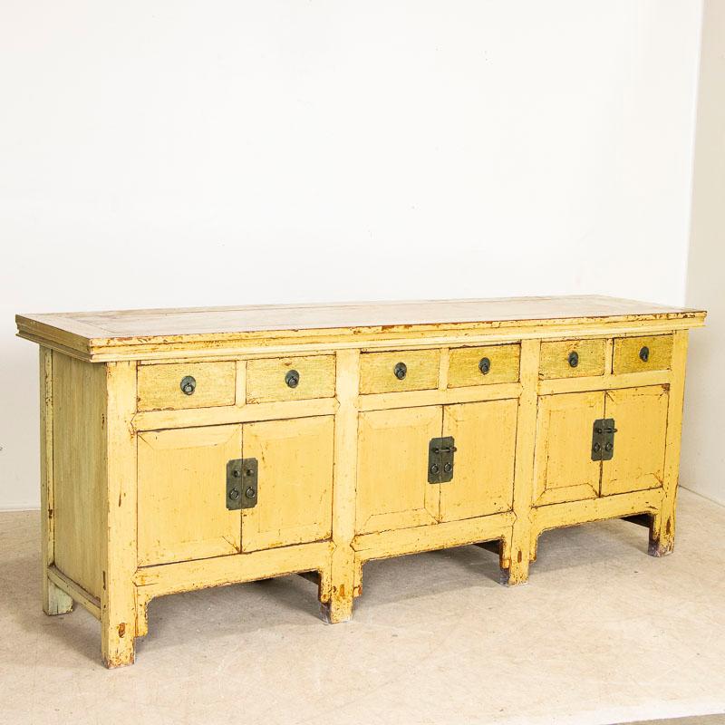 This long Chinese sideboard still maintains its original yellow color and traditional lacquered finish. Note areas where the yellow paint was worn off, revealing the dark hard wood below which adds both character and depth to the stunning finish.