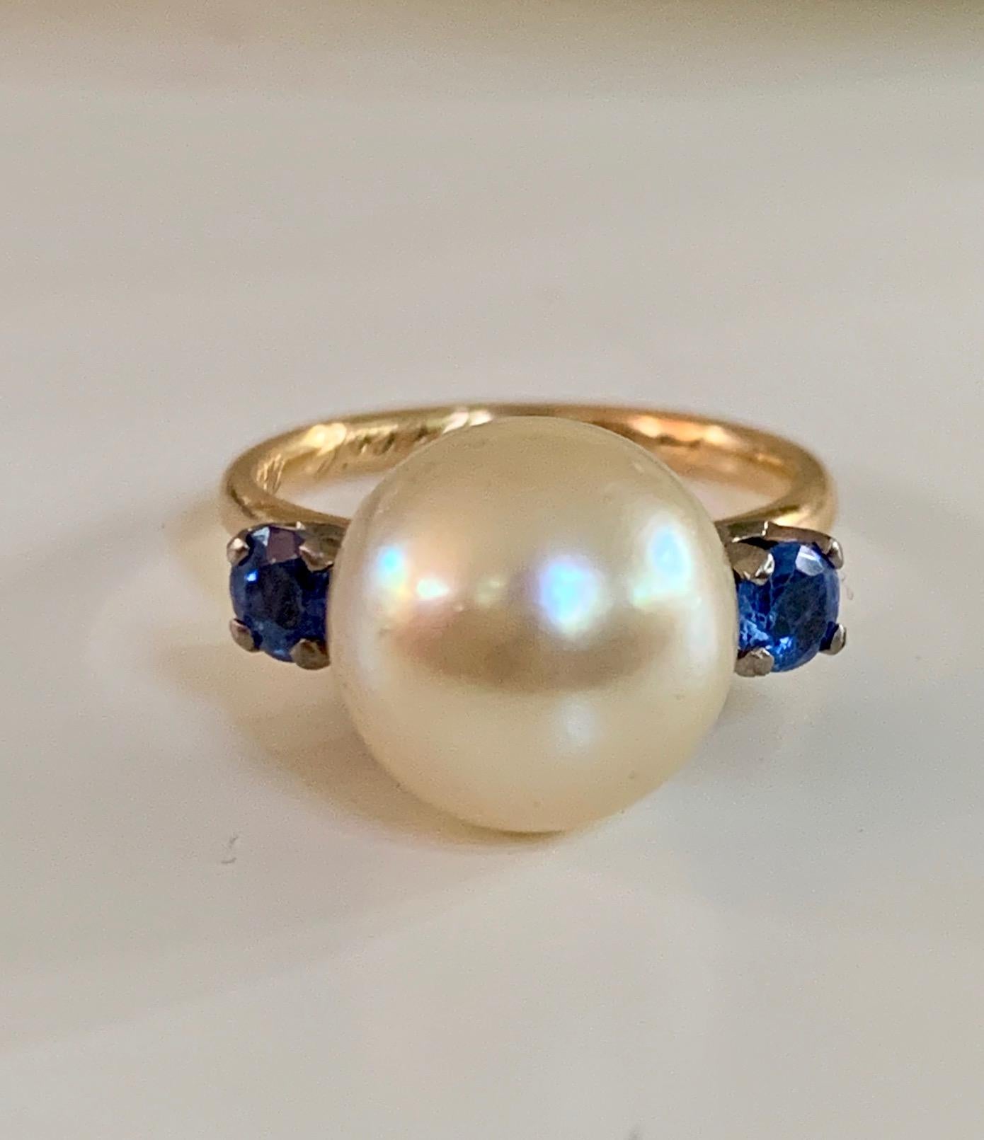 This 11mm Yellow South Sea Pearl 18 karat yellow Gold ring is breathtaking.  The Pearl is beautiful and will definitely turn an eye or two. IT It is accented on both side by a 3.5mm round, faceted, cornflower blue Sapphire.  

Size 5 1/4
Weight: 4.5