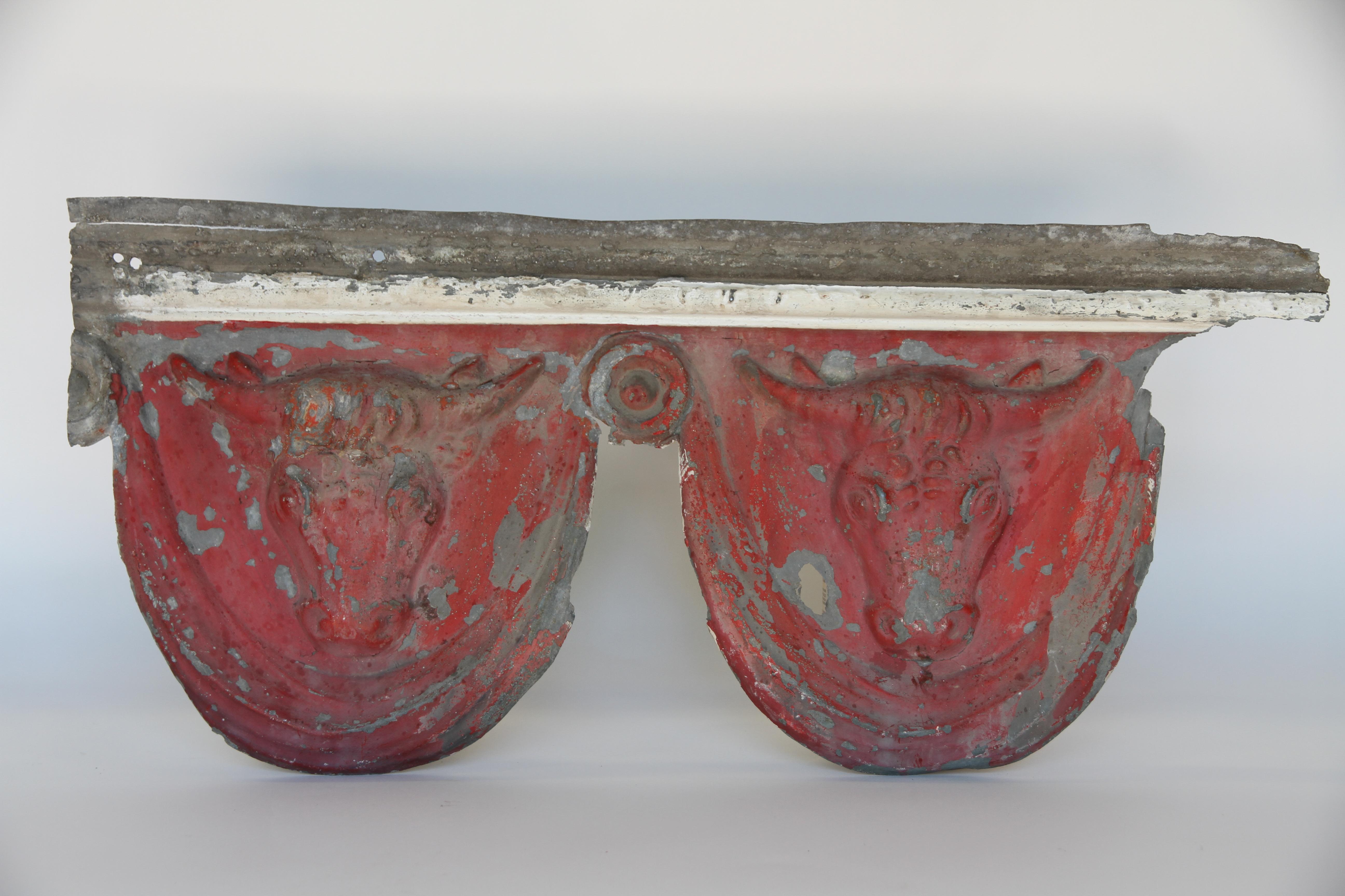 A wonderful antique French architectural zinc element with two bull heads embossed into the piece. One side has red paint and the other side has remnants of white. This is probably a small piece of exterior or interior crown molding of a barn or