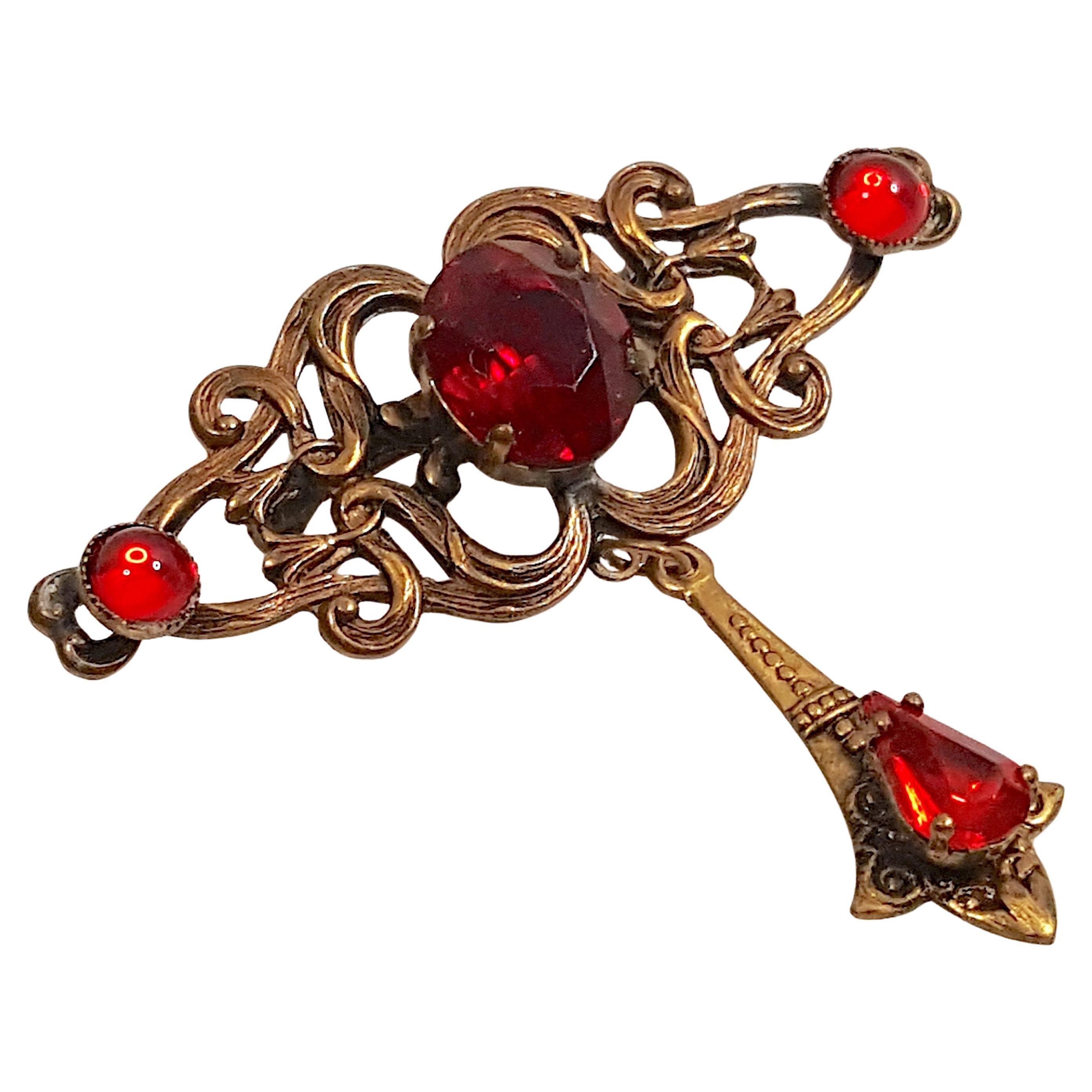 In the 1920s in an Art-Nouveau style, Czech costume-jewelry designer Max Neiger created this brass dangle brooch that features three different shapes of either bezel-or-prong set red glass for a wide variety of rich and bright reflections. Aside