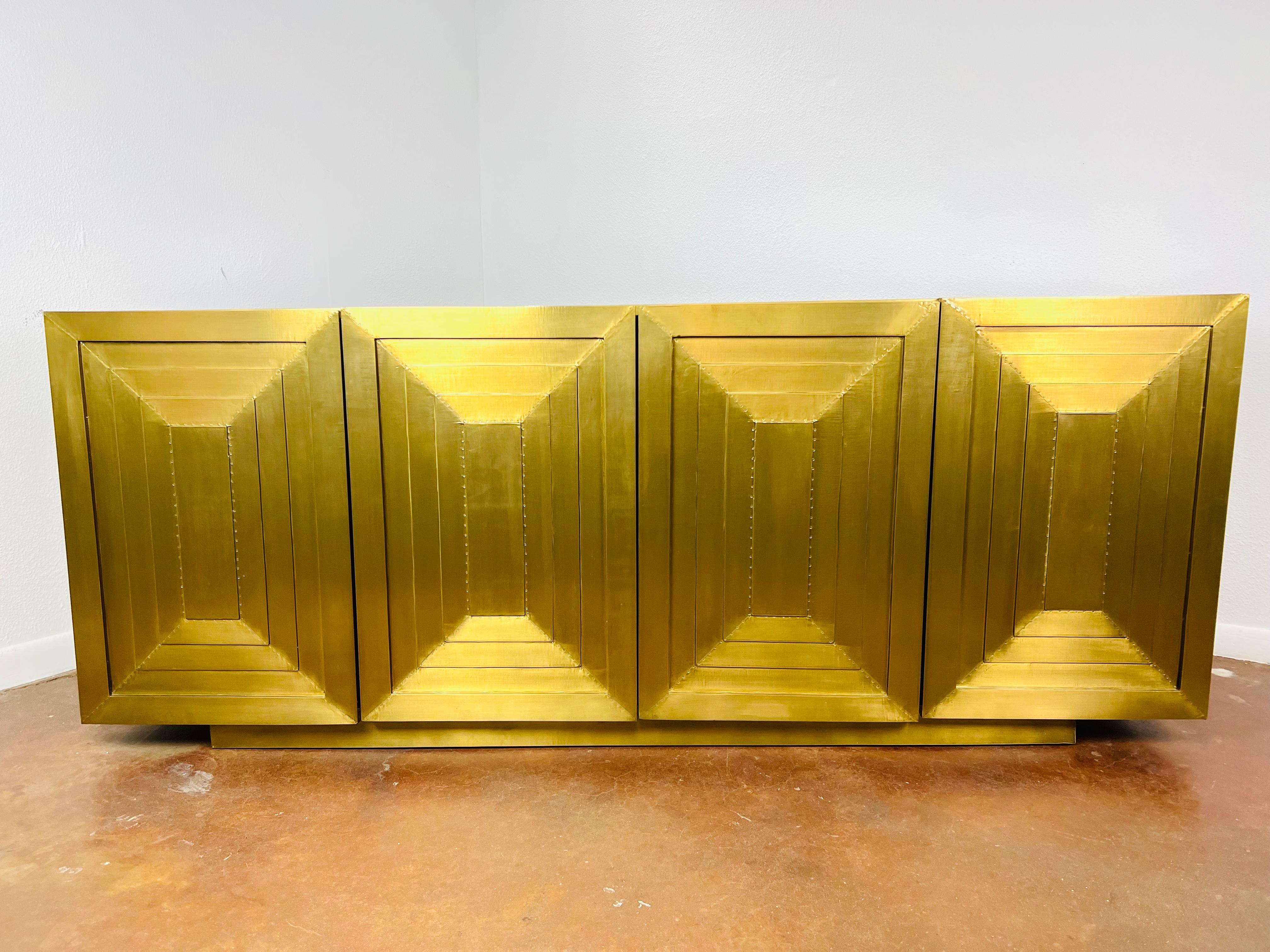 Crafted from mango wood, this blocky buffet is clad in sheets of antiqued brass, accented by tiny tack details. The 