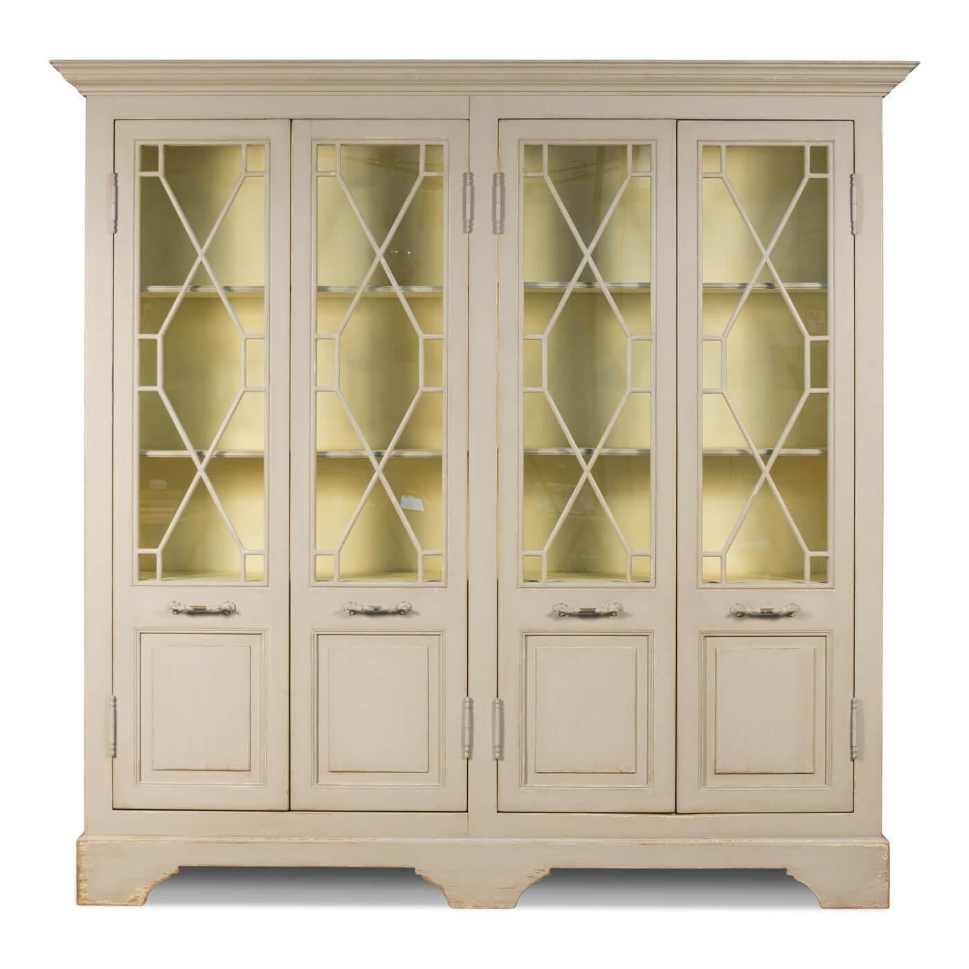 Antiqued farmhouse style painted four-door cabinet. A beautiful and functional cabinet that can be used for display and storage. The exterior is painted in soft tones, beautiful fretwork glass doors reveal the interior is painted in light butter