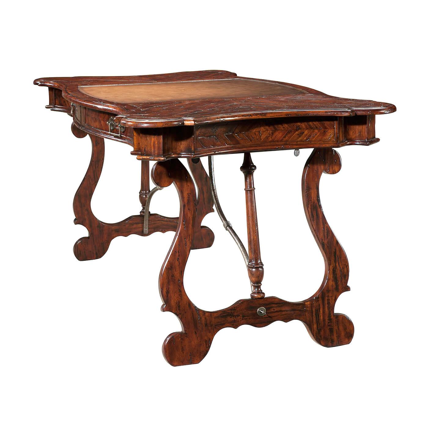 An antiqued mahogany writing table, the serpentine parquetry planked top inset with a central burnished leather writing surface, above two frieze drawers, on splayed lyre supports with a baluster turned central support, joined by wrought iron