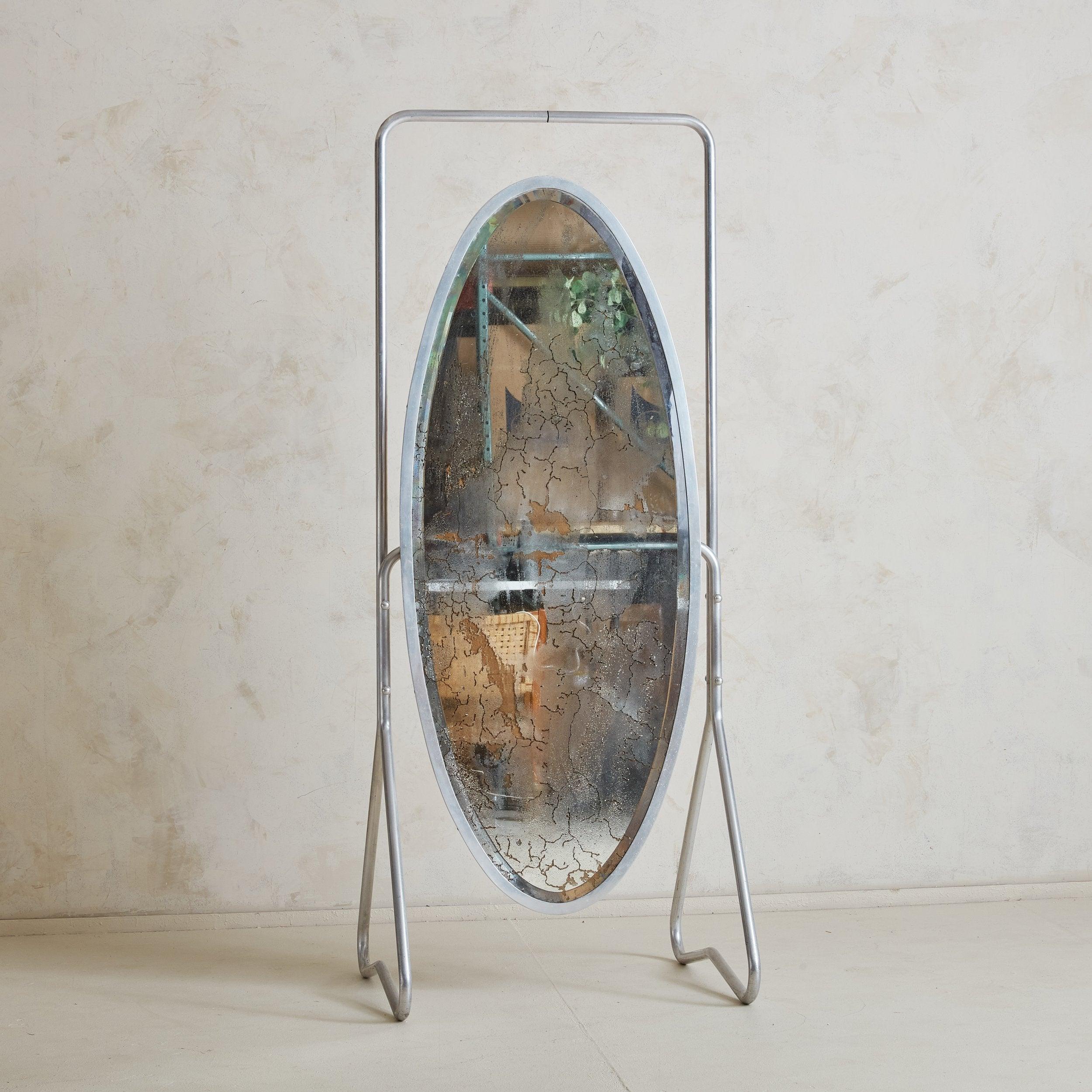 A French silver mercury glass freestanding floor mirror from the 1930s. The original antiqued oval mercury mirror glass displays a gorgeous crackle design throughout. An industrial double pedestal chrome frame supports the mirror, adding a floating
