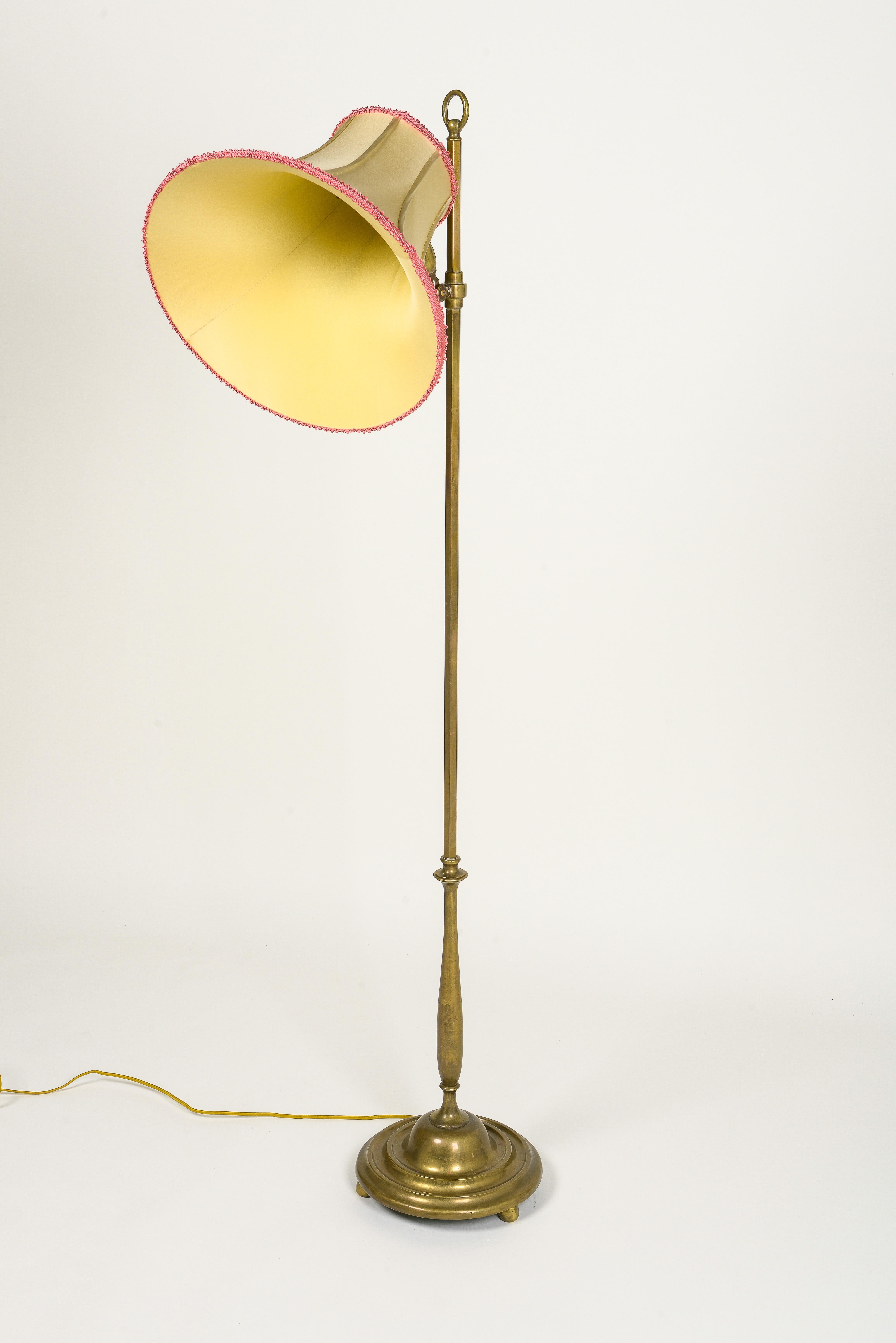 The turned adjustable columnar with angled light fitted with one bulb socket; on a turned round base on ball form feet. With gold silk bell lamp shade trimmed in soft red.