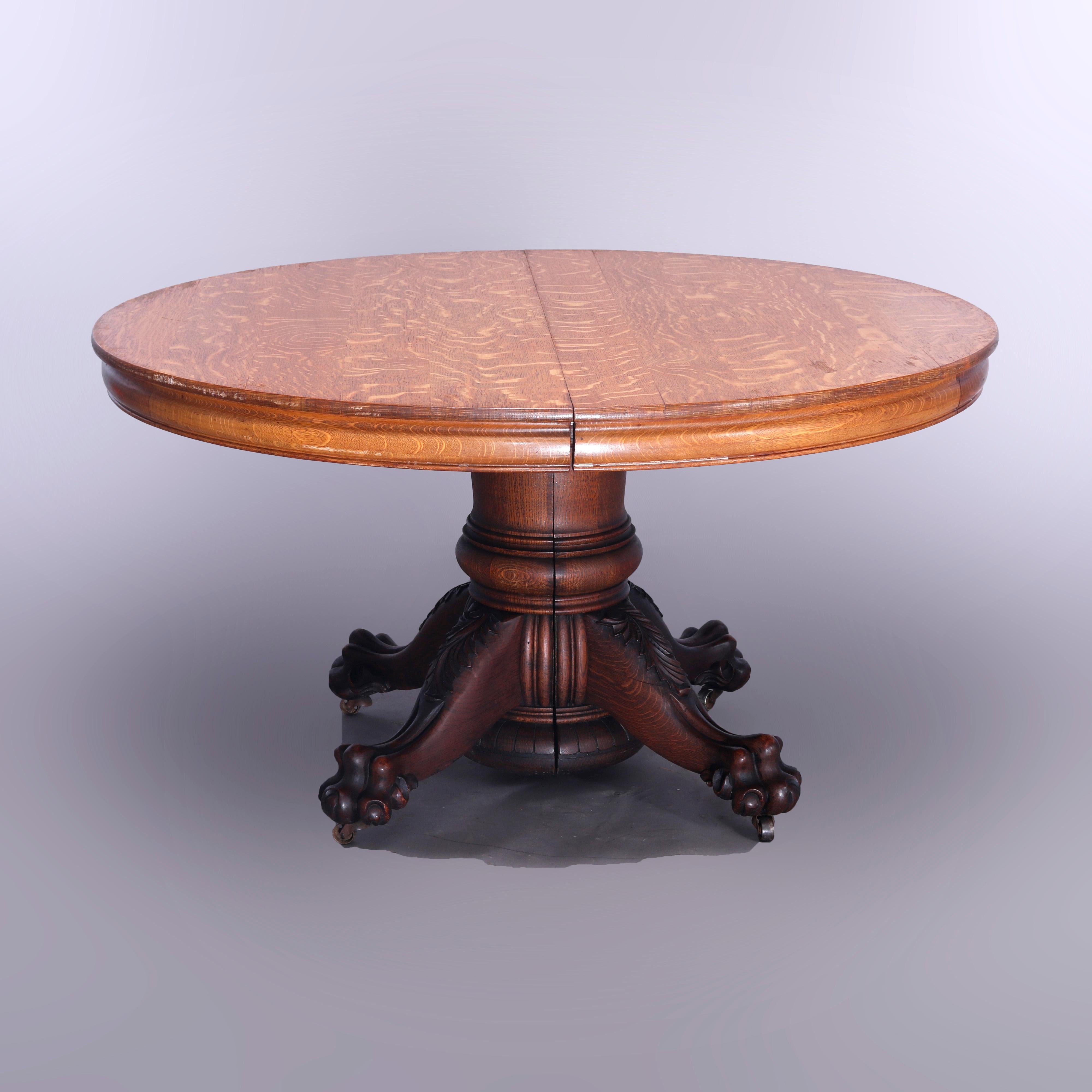 An antique banquet dining table attributed to Hastings offers quarter sawn oak construction with round top over split pedestal base raised on cabriole legs terminating in carved paw feet, accepts up to and includes five leaves with central support