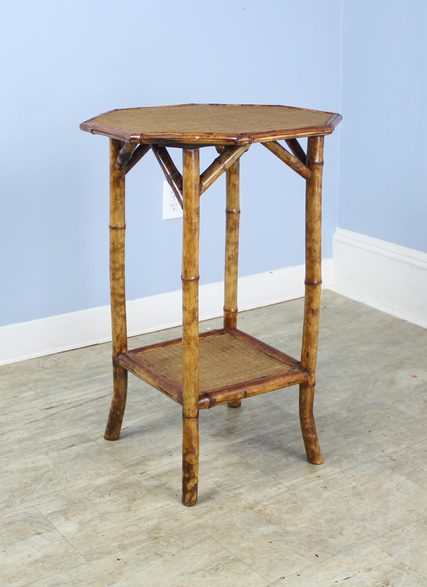 An antique English bamboo side table, with flared legs and with and an unusual octagonal top. Both shelves are made of tightly woven rattan that is in very good condition. The bamboo, vividly painted, is in good sturdy condition. Charming as an end