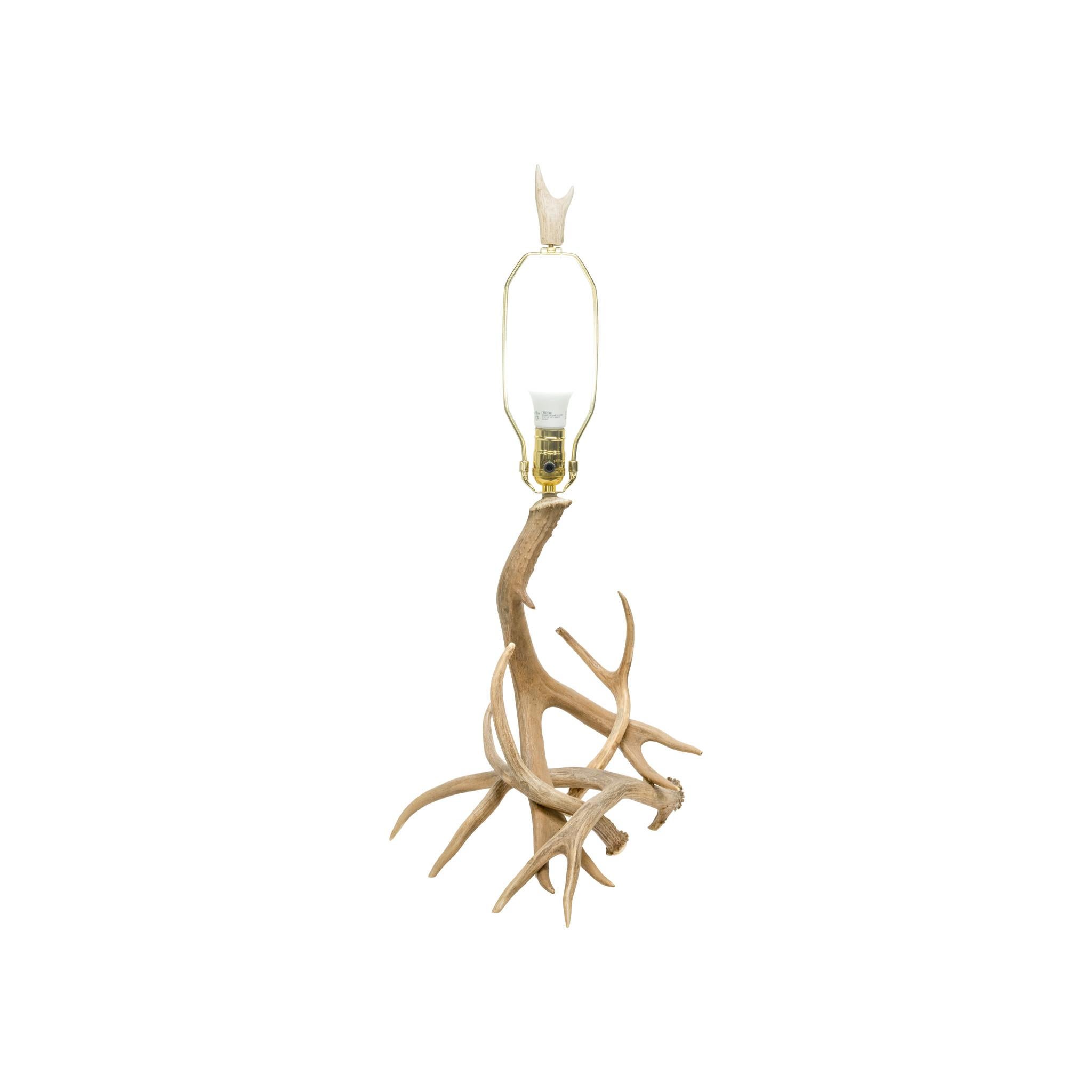 Natural antler table lamp. Featuring three antlers comprising base and oil painted shade with antler finial and brass-colored hardware. Simple, elegant design, great for a rustic or modern cabin. Antlers are a warm, light beige tone with some