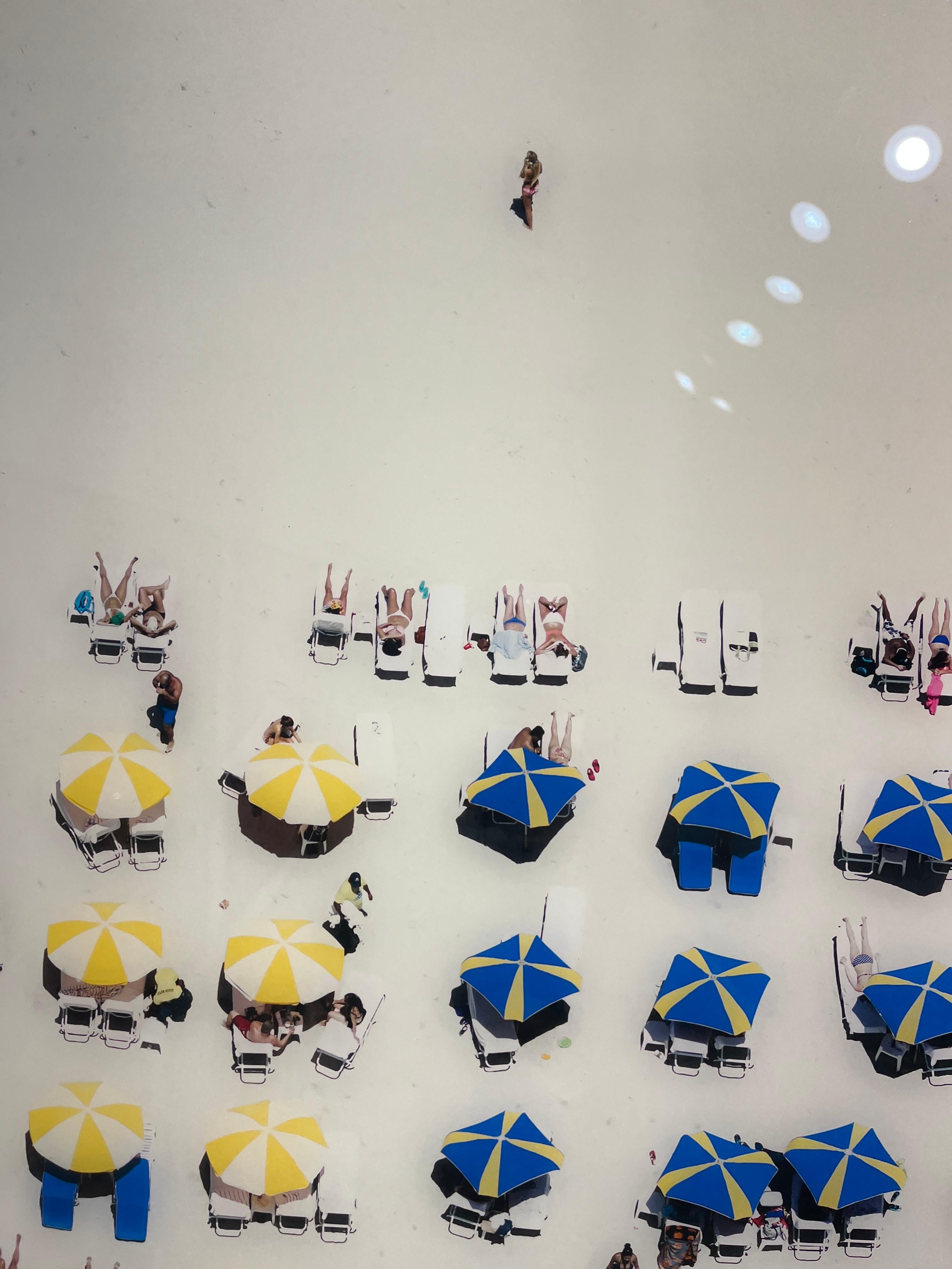 By hanging out of a helicopter hovering 300 feet in the air, Antoine Rose uniquely captures the Hamptons from a sharp 90 degree angle. This piece is a snapshot of shared beach activities that features colorful accessories and gorgeous blue-green